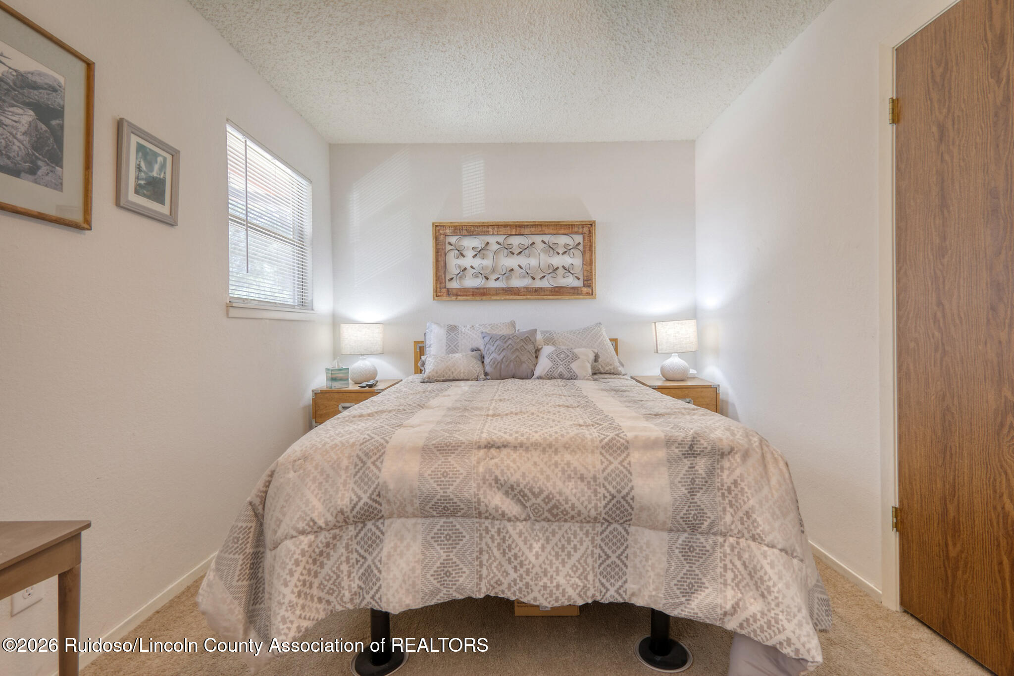 Furnished bedroom with a patterned bed, matching nightstands, lamps, and framed wall art.