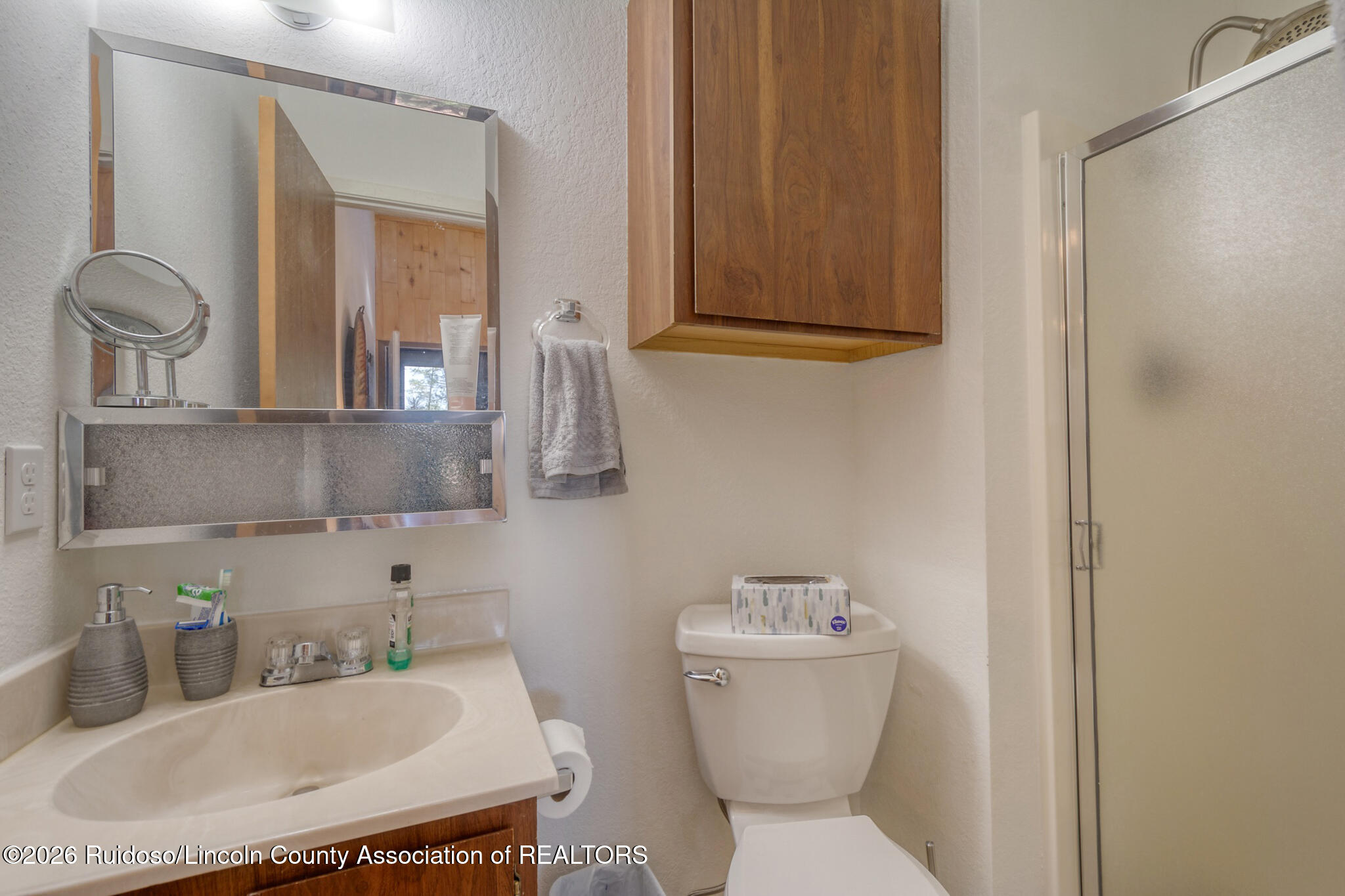 Bathroom with cream vanity, wooden cabinet, and glass-enclosed shower.
