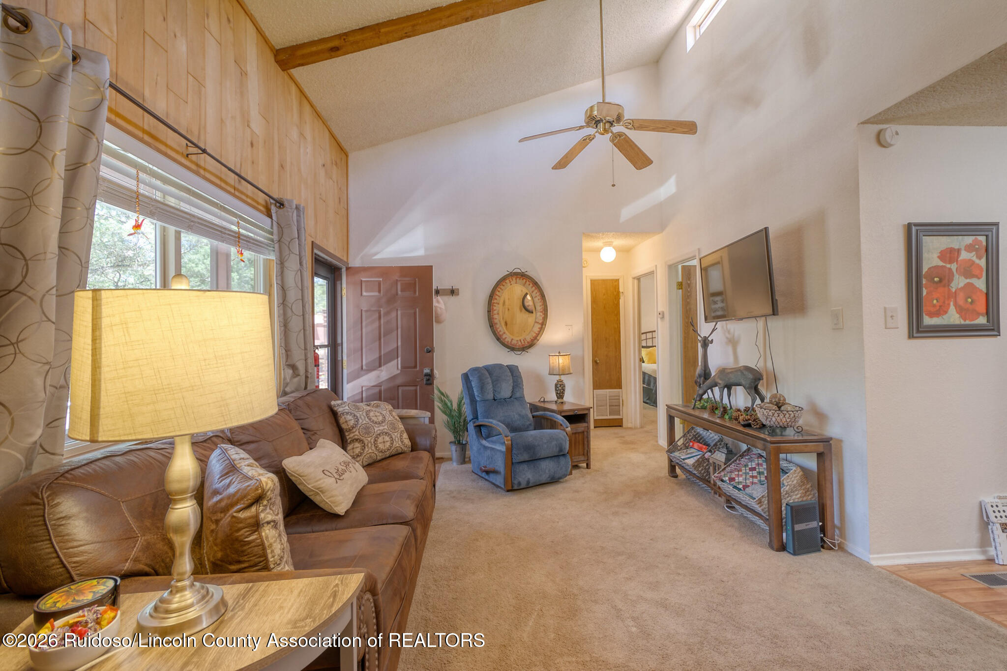 Furnished living room with vaulted ceiling, wood-paneled wall, leather sofa, blue recliner, and wall-mounted television.