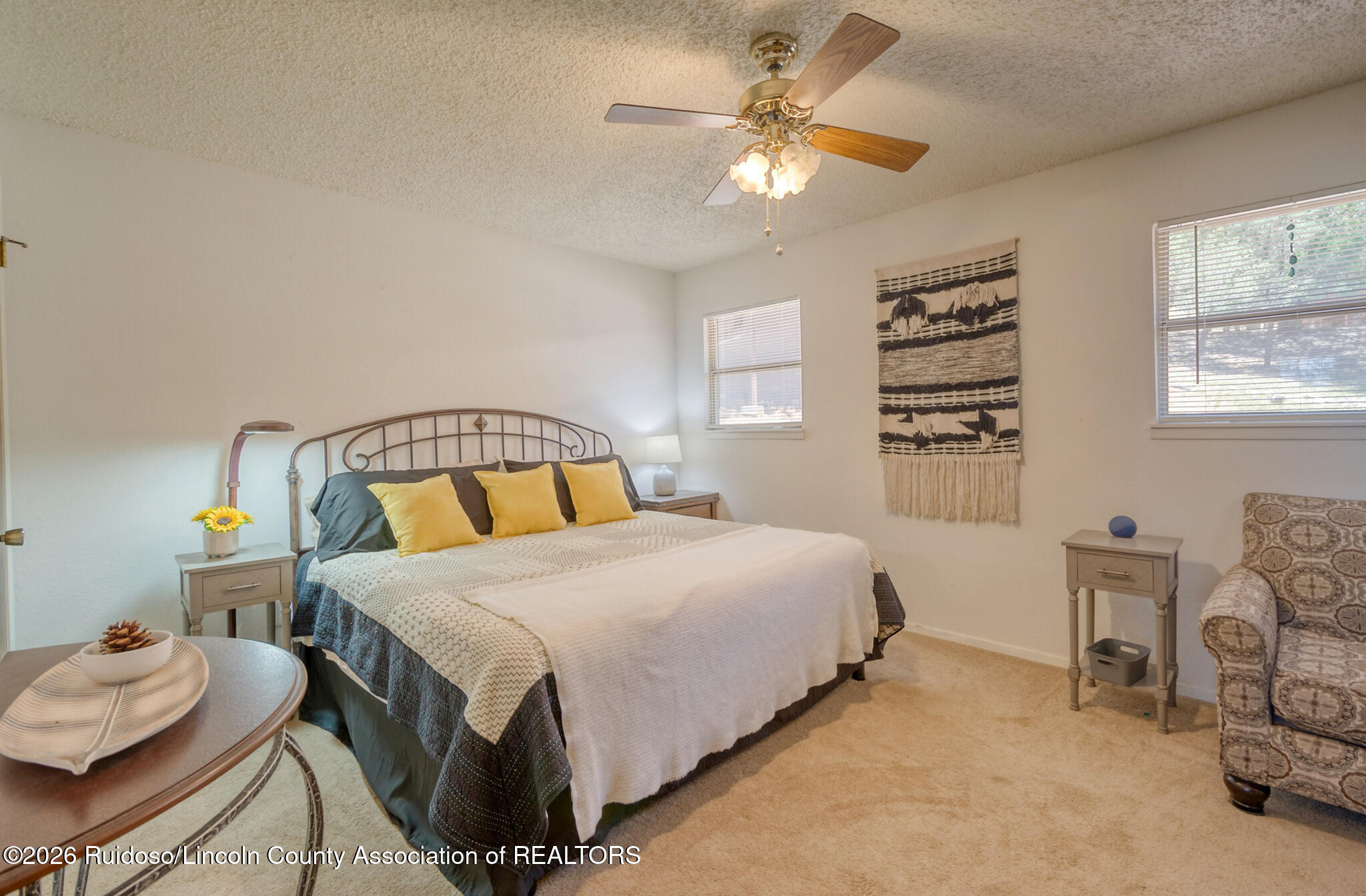 Furnished bedroom with a large bed, yellow pillows, ceiling fan, and patterned armchair.