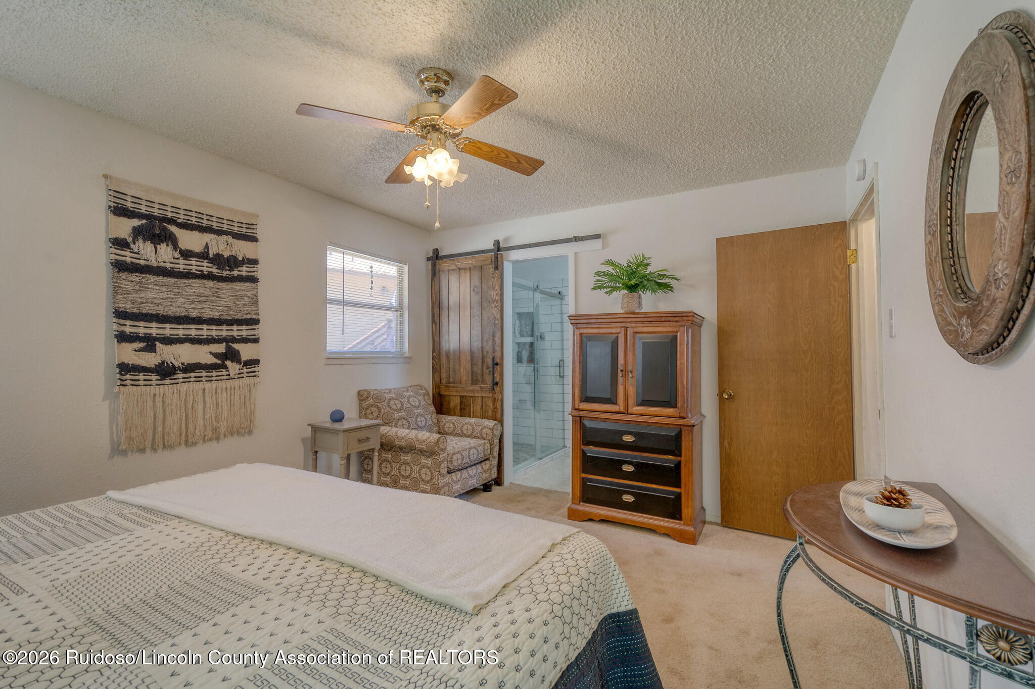 Bedroom with a patterned bed, wooden cabinet, and glass-enclosed shower.