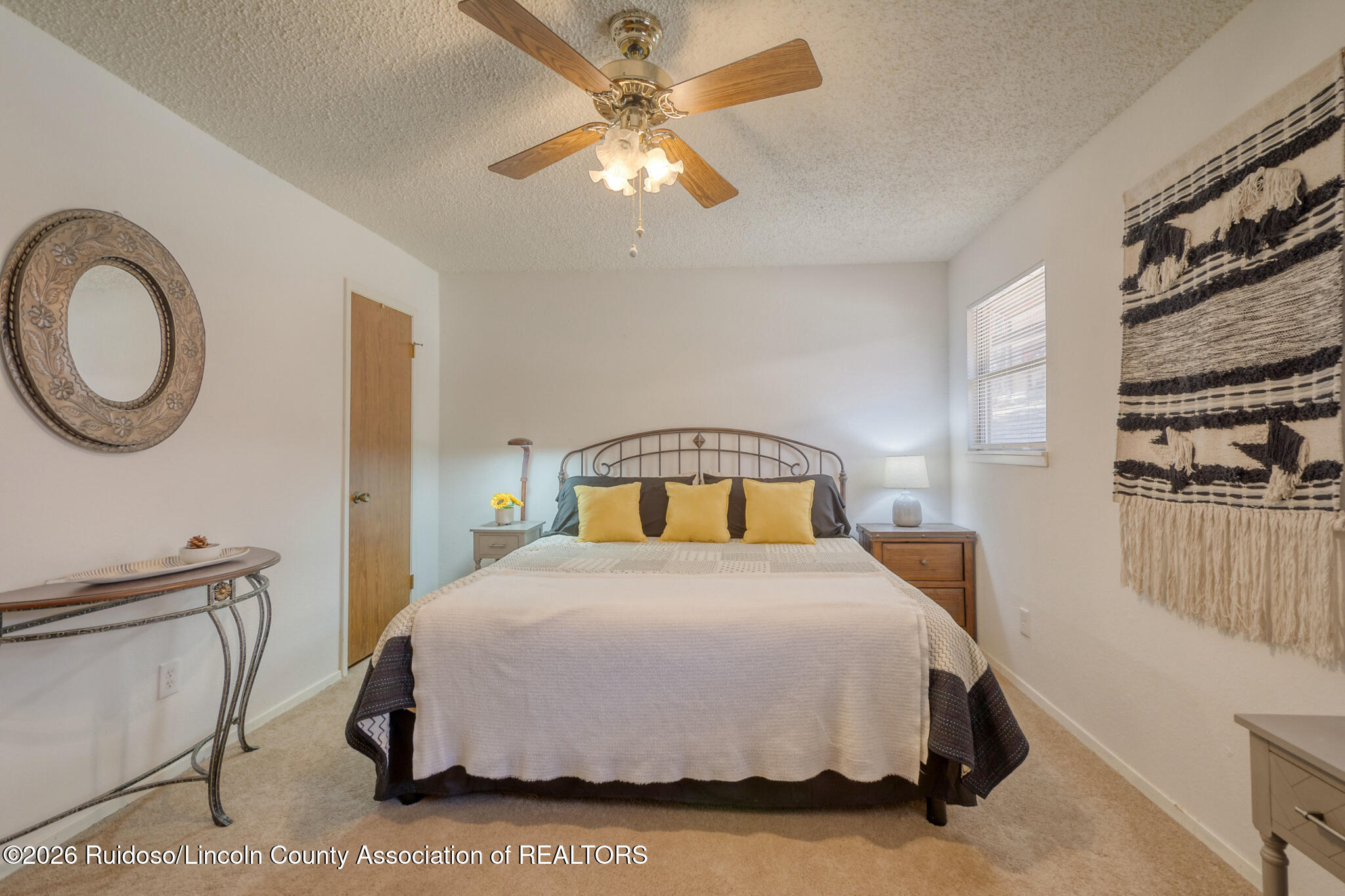 Furnished bedroom with a metal-frame bed, yellow accent pillows, wooden nightstands, and ceiling fan.