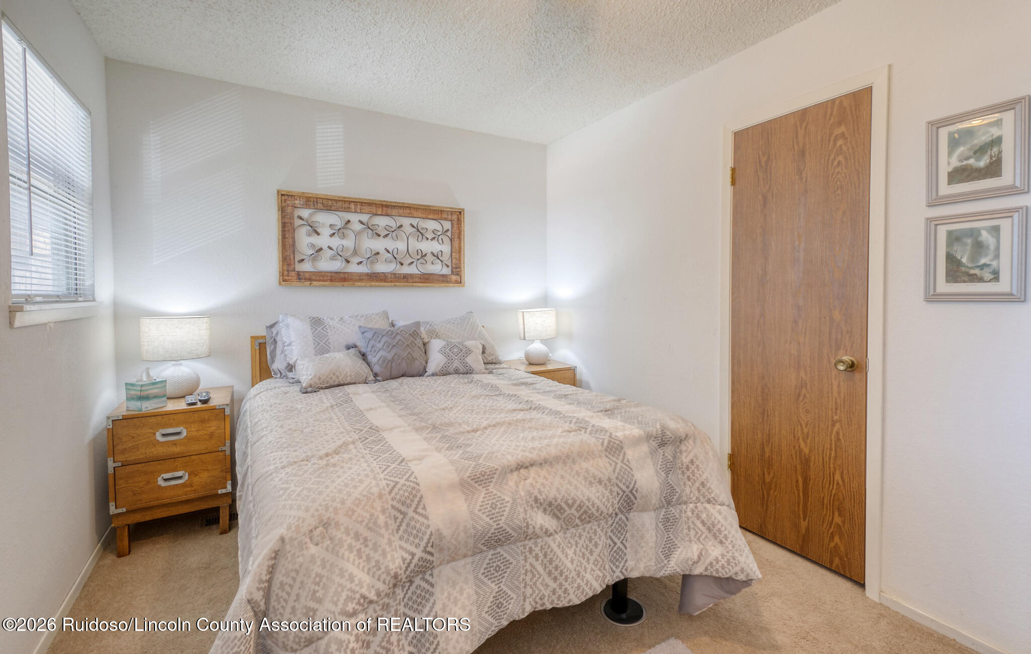 Furnished bedroom with a pale patterned bedspread, wooden nightstands, and framed wall art.