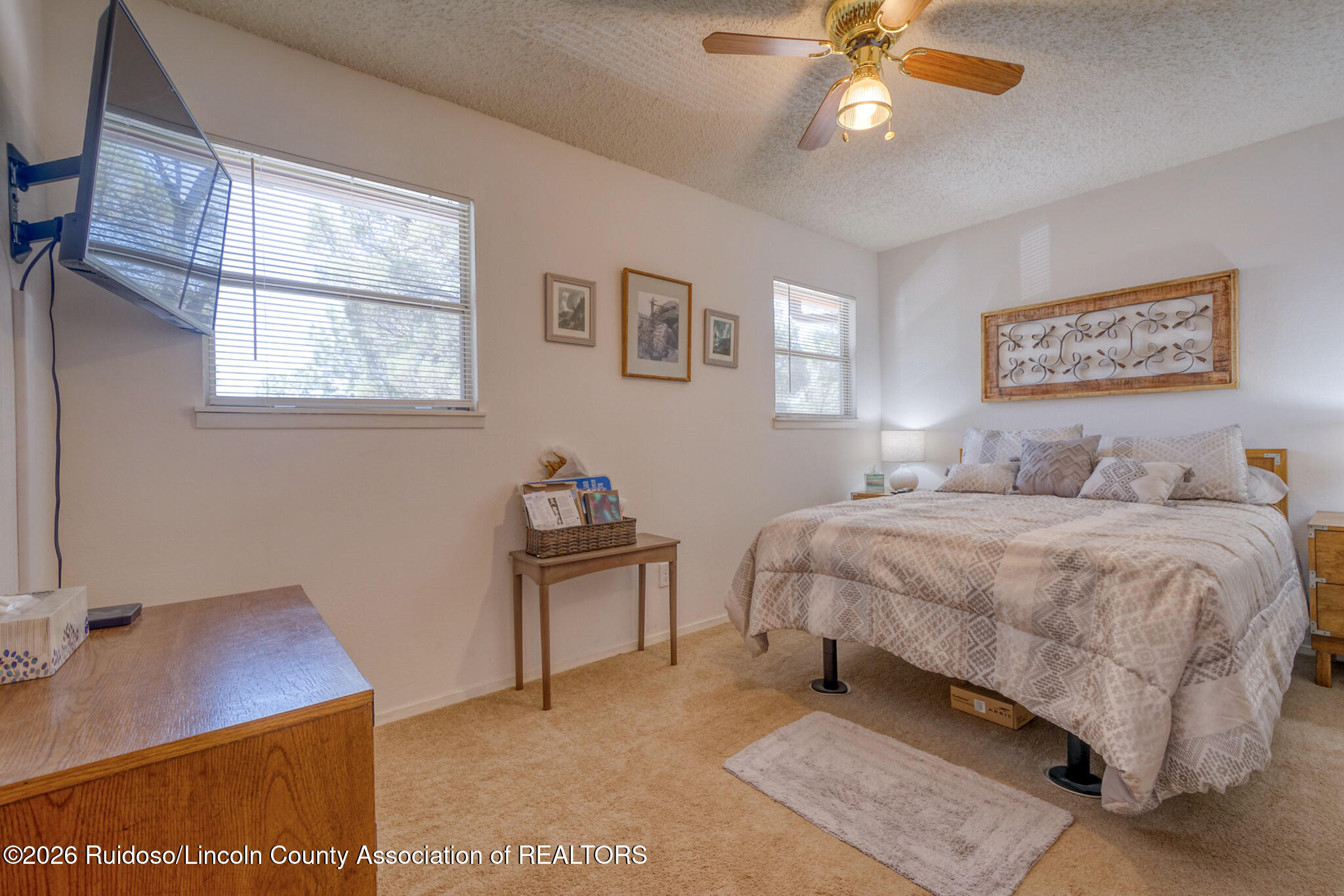 Bedroom with a patterned bedspread, wall-mounted television, and ceiling fan.