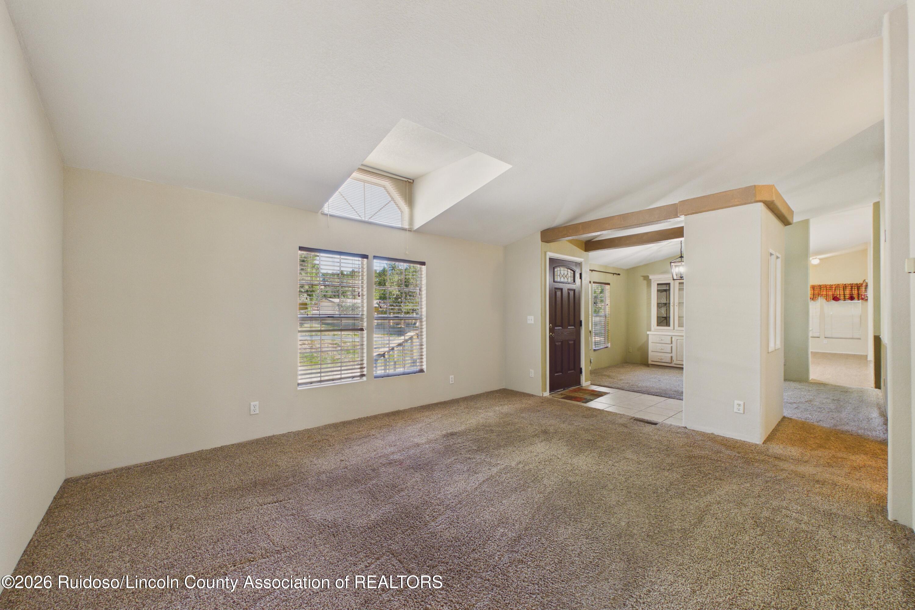 Vacant carpeted living room with a skylight, two windows, and an open entryway.