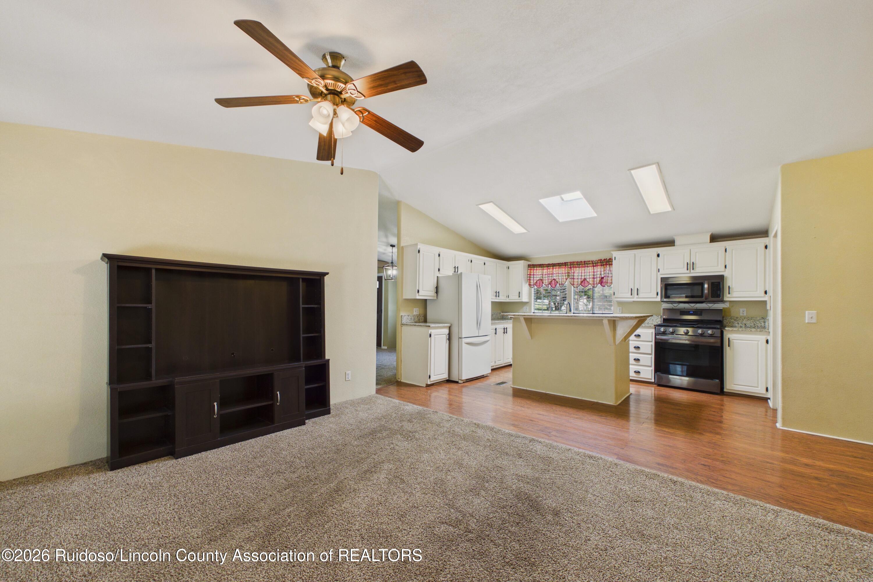 Open living room and kitchen with vaulted ceiling, white cabinetry, breakfast counter, and ceiling fan.