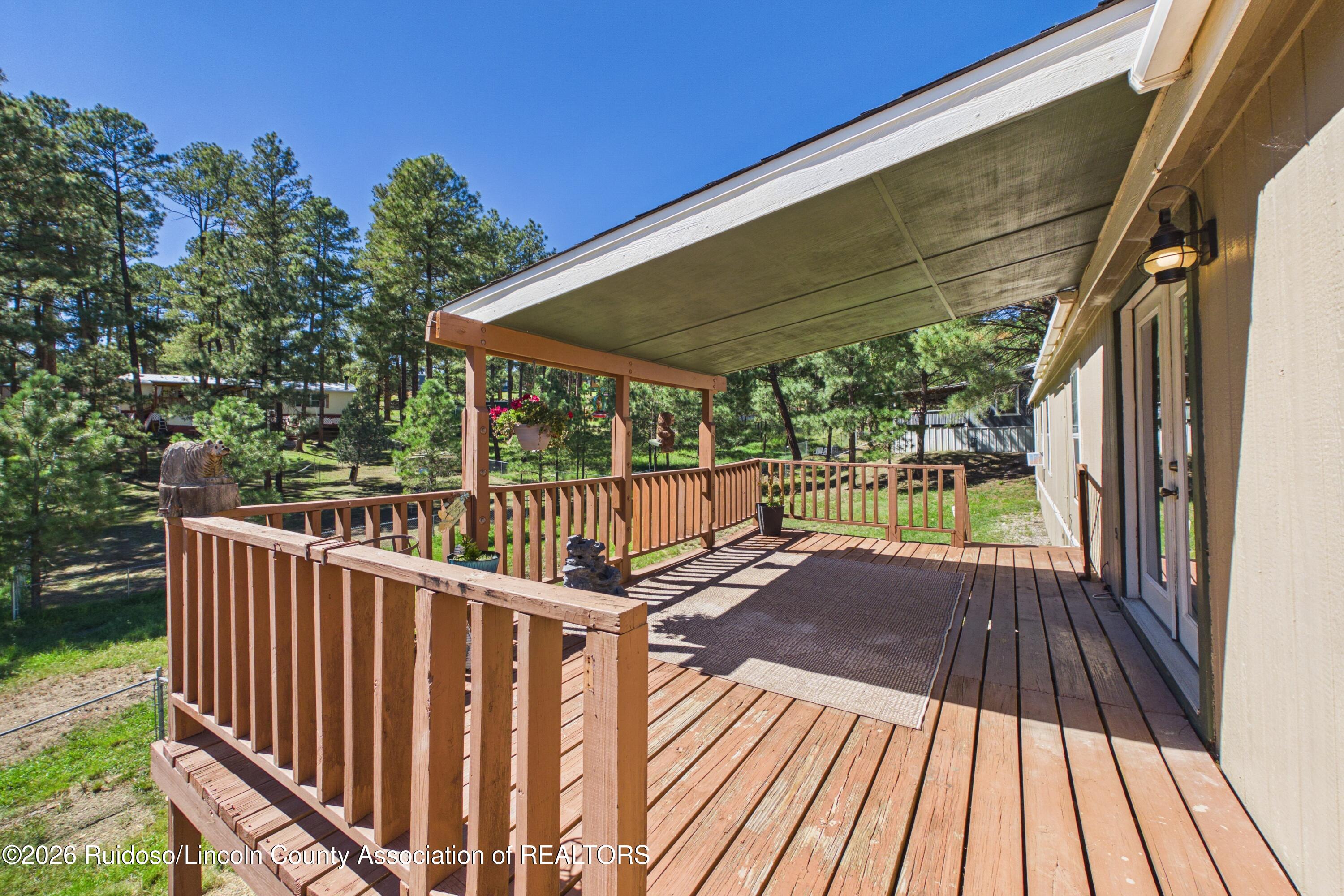 Covered wooden deck with railings and planters overlooking a pine-filled yard.