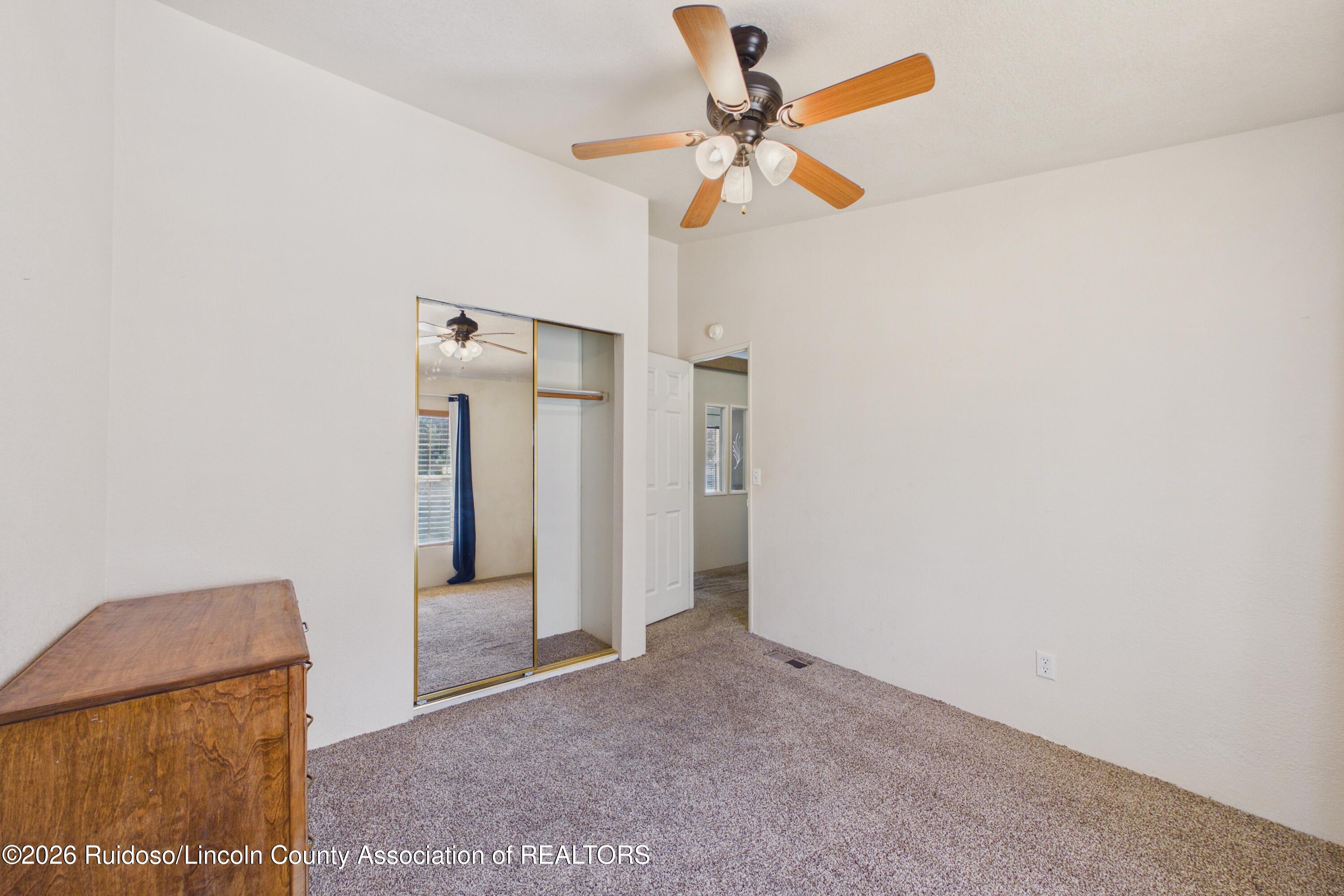 Bedroom with mirrored sliding closet doors, beige carpet, and a wooden ceiling fan.