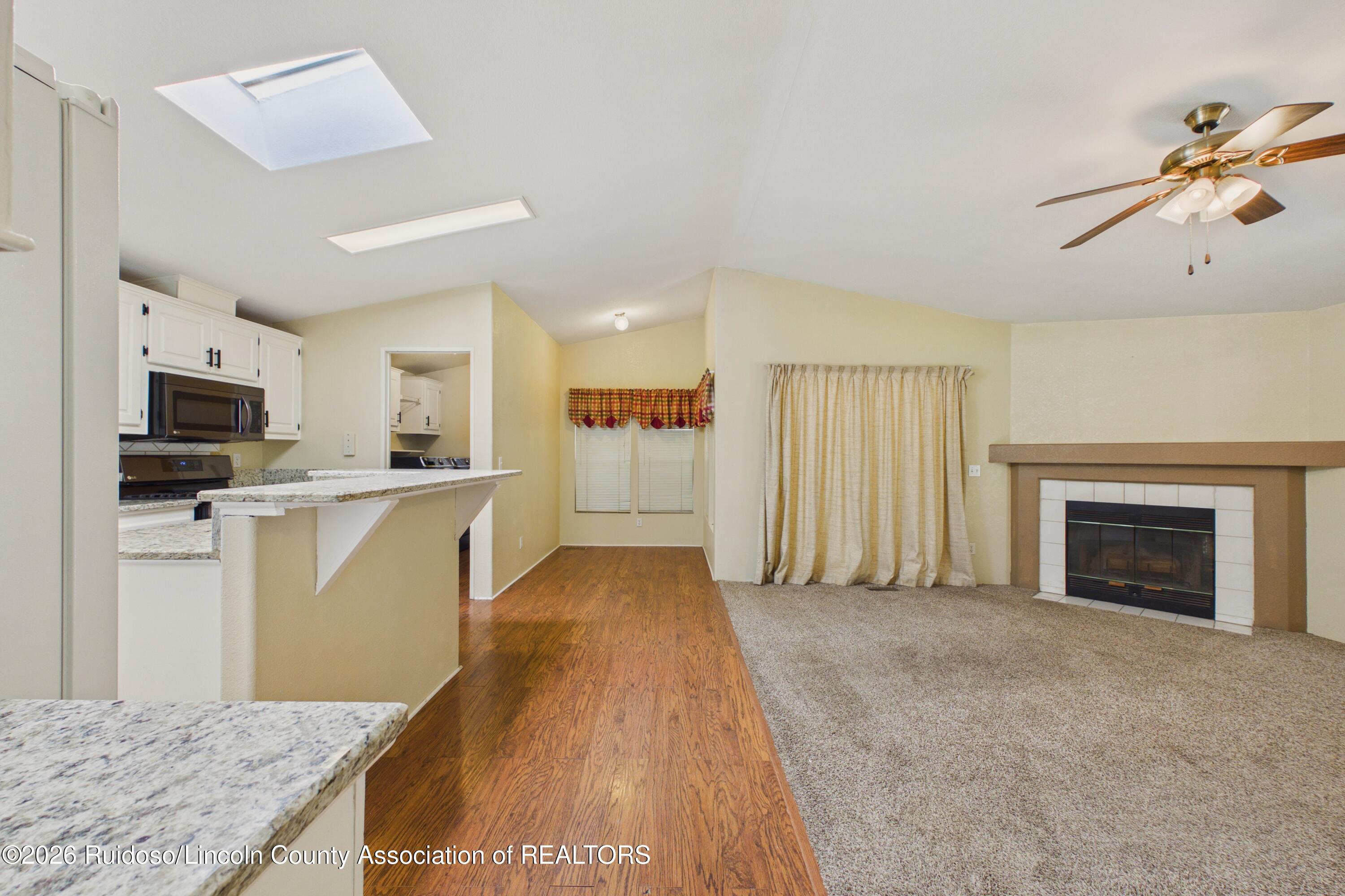 Open living room and kitchen with granite counters, wood-look flooring, and a fireplace.