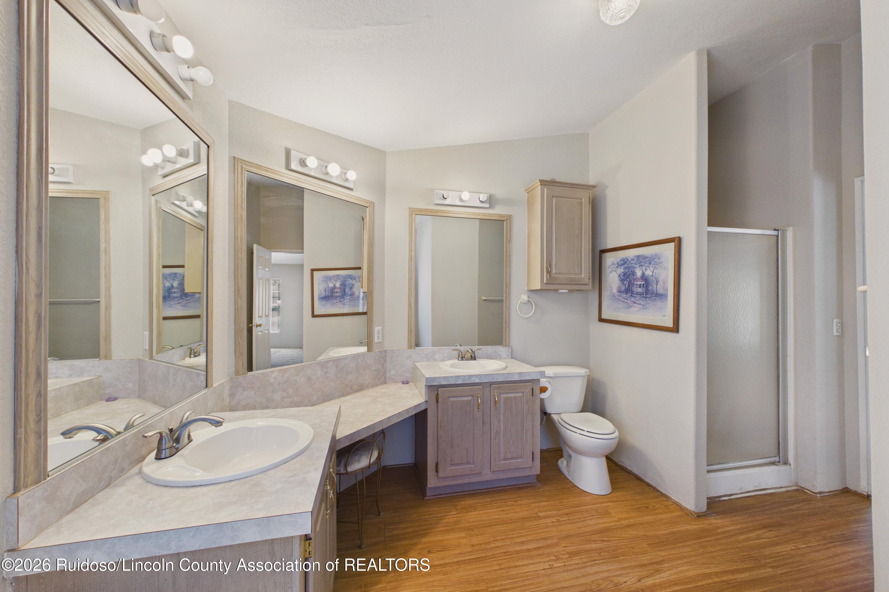 Spacious bathroom with two sink vanities, large mirrors, a toilet, and a frosted-glass shower.