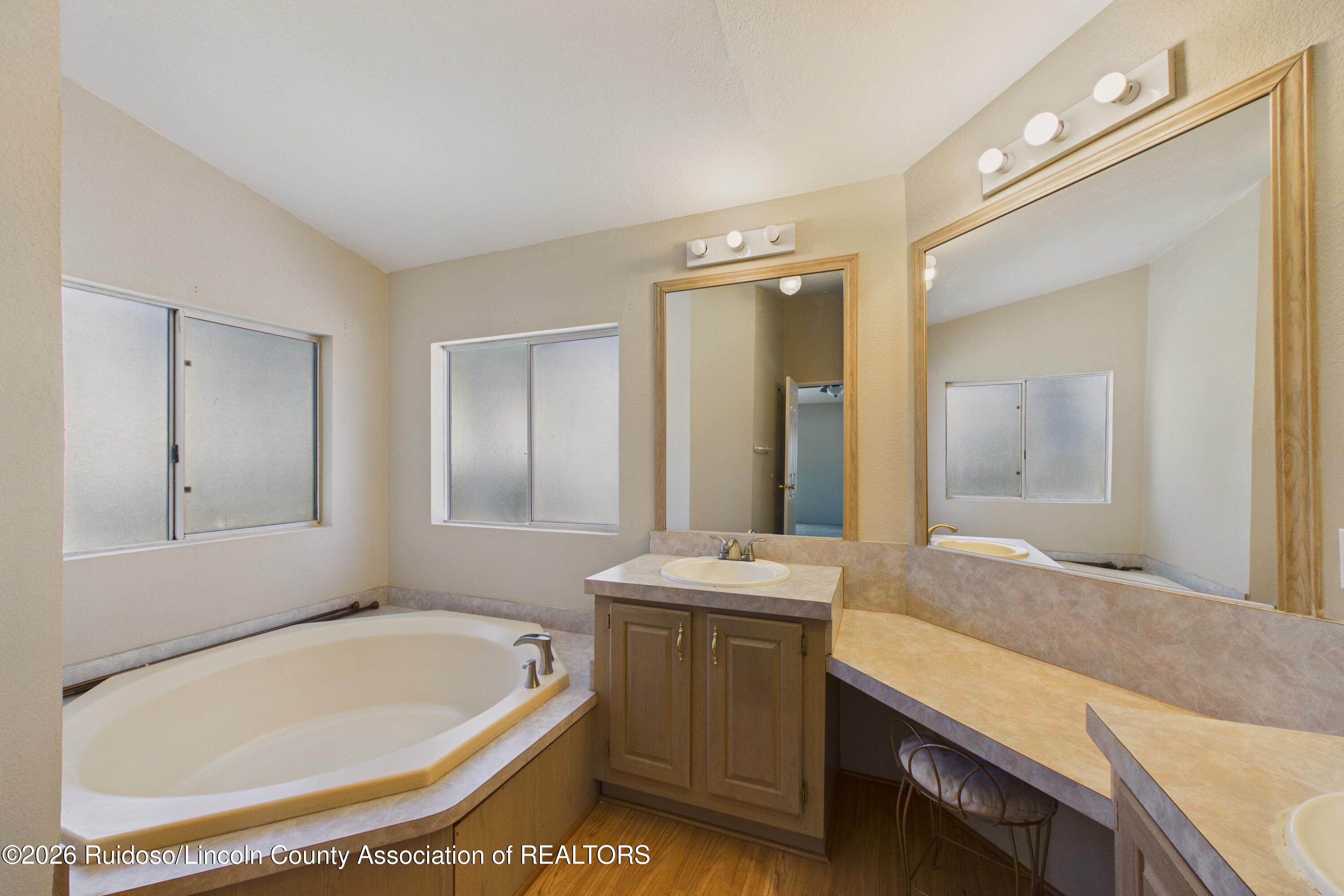Bathroom with a built-in corner tub, wood vanity, and long mirrored countertop.