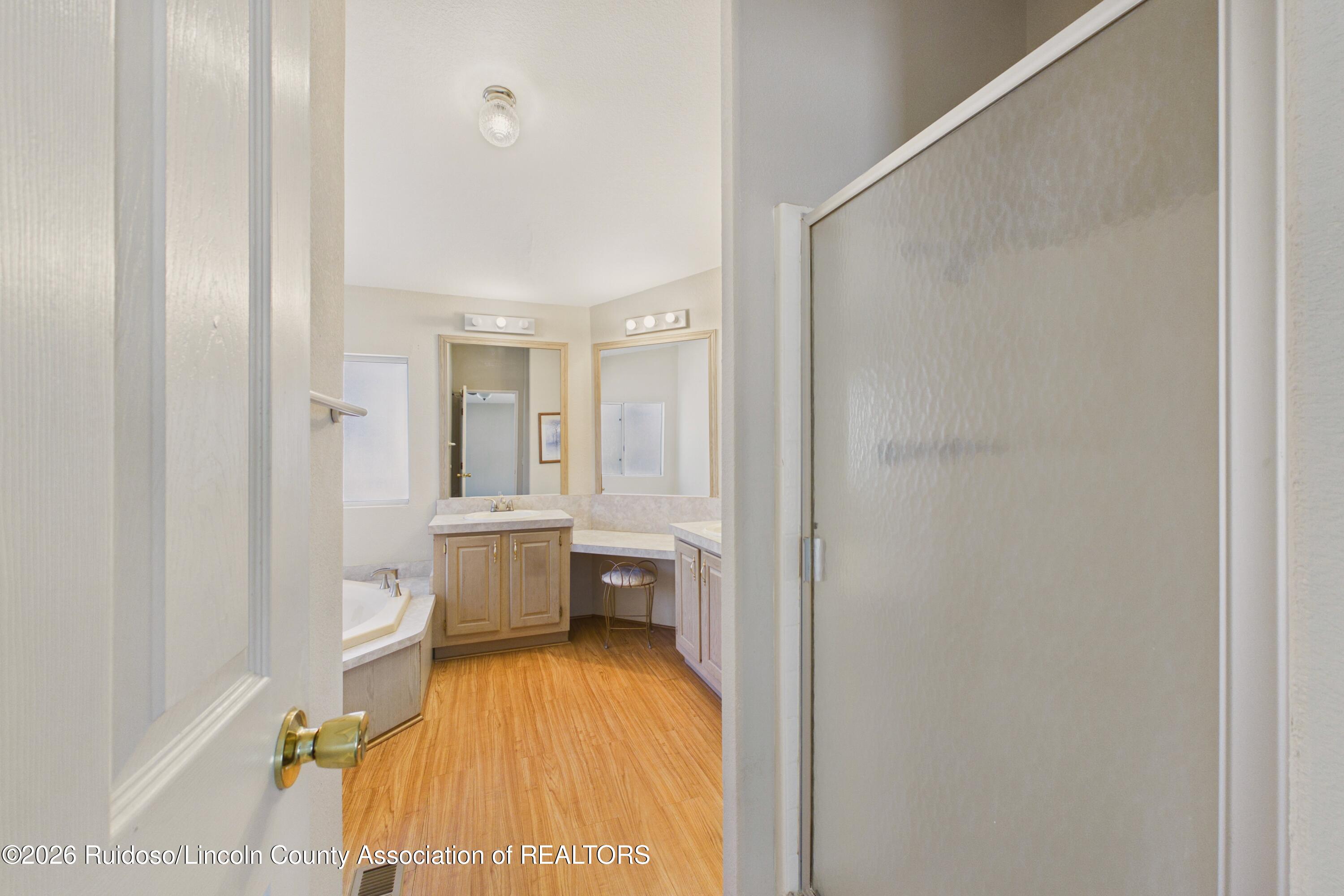 Bathroom with corner soaking tub, vanity, large mirrors, and wood-look flooring.