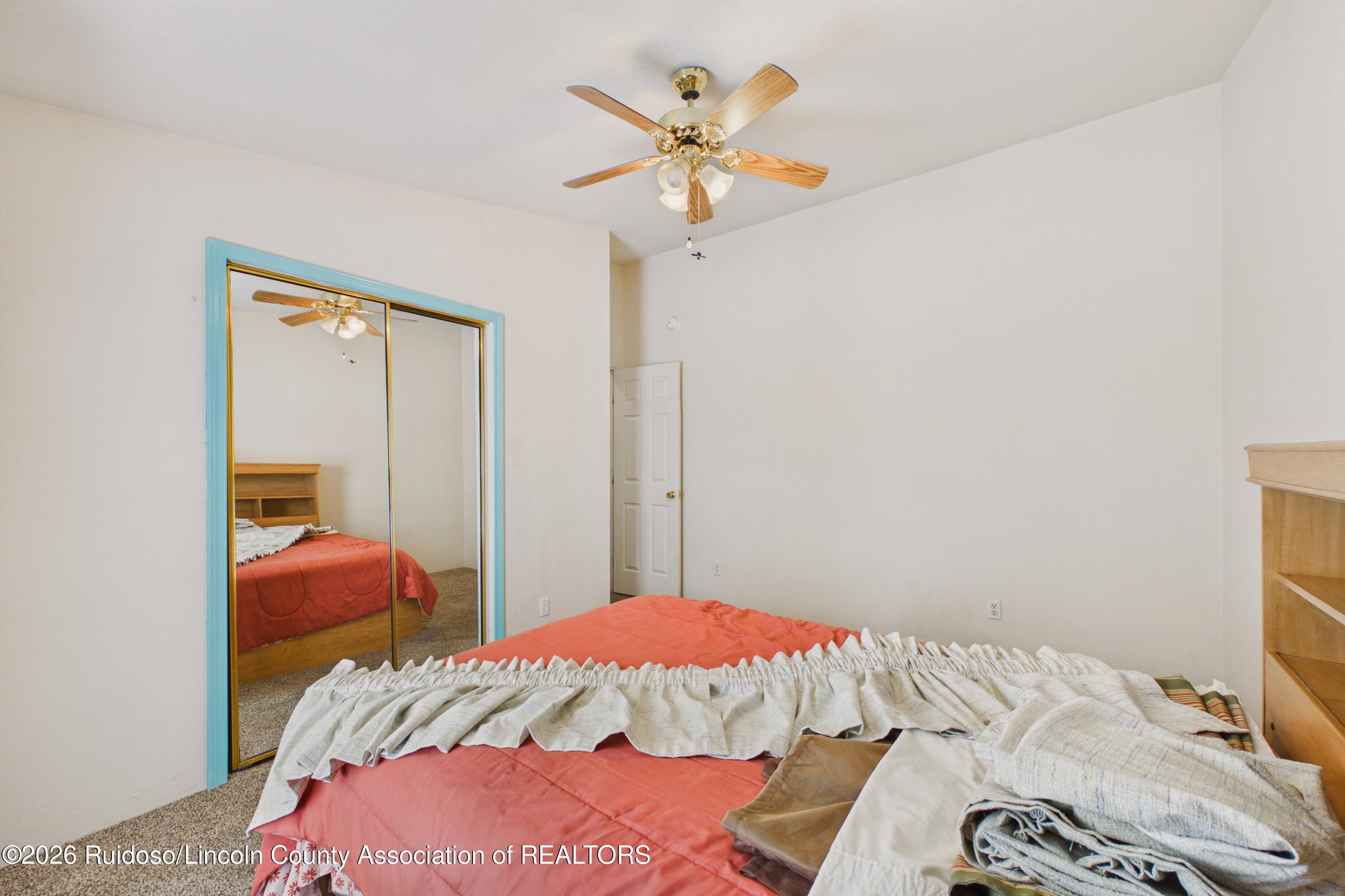 Bedroom with coral bedding, mirrored closet doors with turquoise trim, and a wooden ceiling fan.