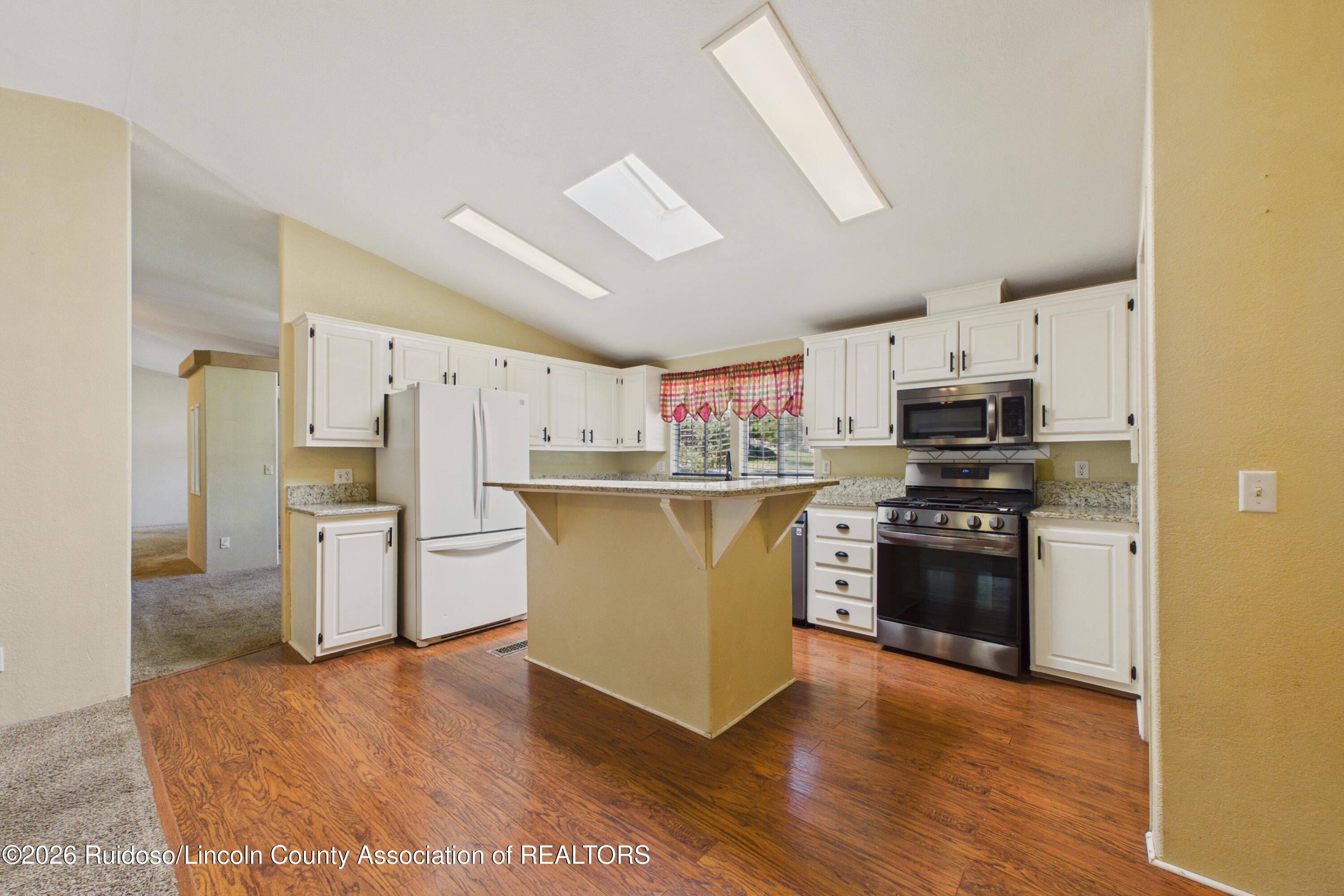 Kitchen with white cabinetry, granite counters, a central breakfast bar, and wood flooring.