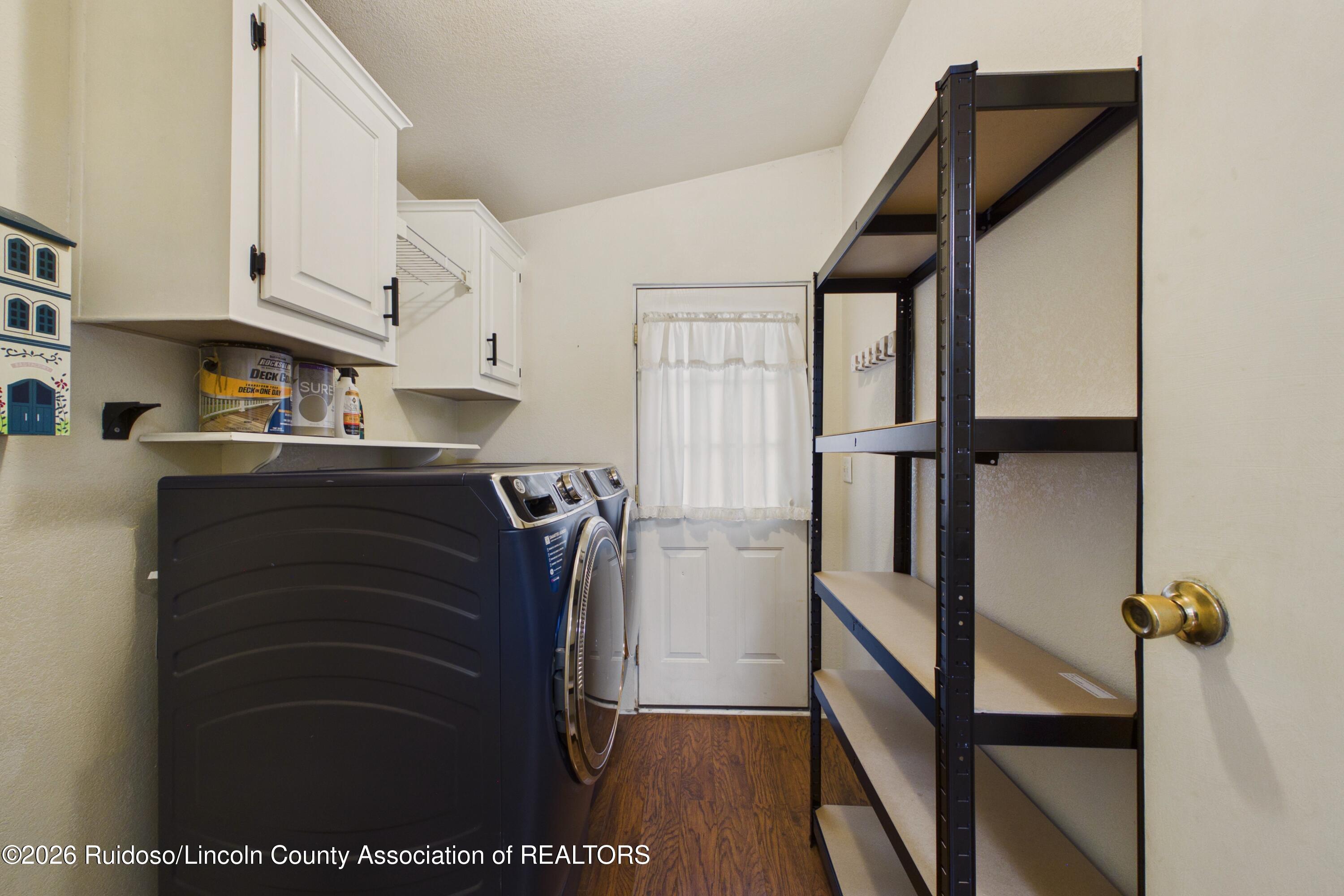 Laundry room with dark front-loading washer and dryer, white cabinets, and open shelving.