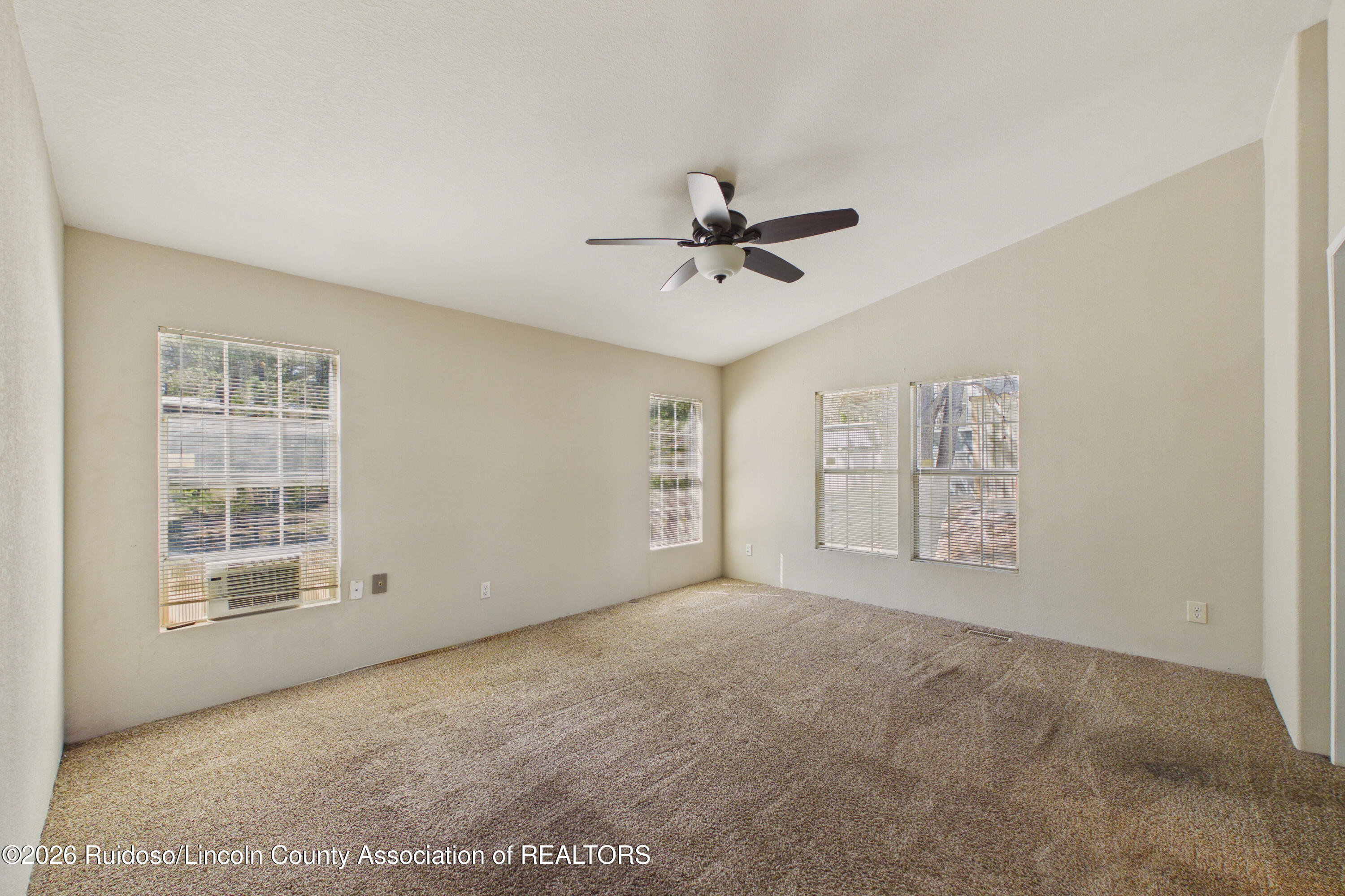 Empty carpeted bedroom with several blinded windows, a window air conditioner, and a ceiling fan.