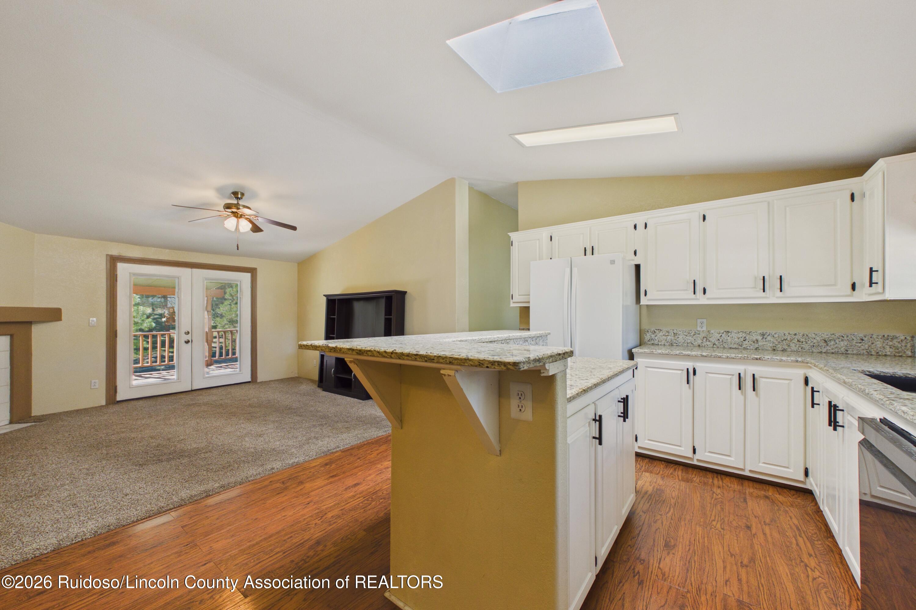 Kitchen with white cabinets and granite peninsula opening to carpeted living area with deck doors.