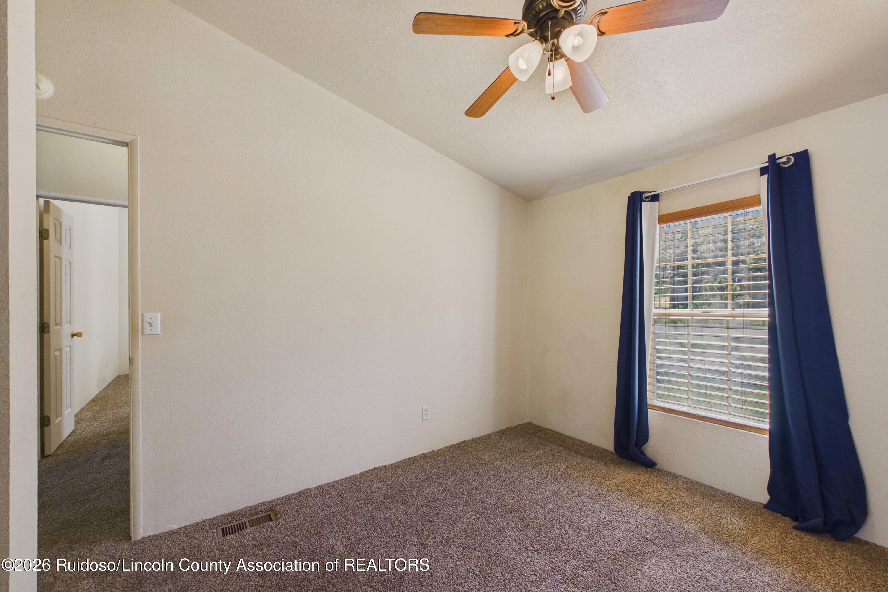 Empty bedroom with beige carpet, a ceiling fan, and a window framed by navy curtains.