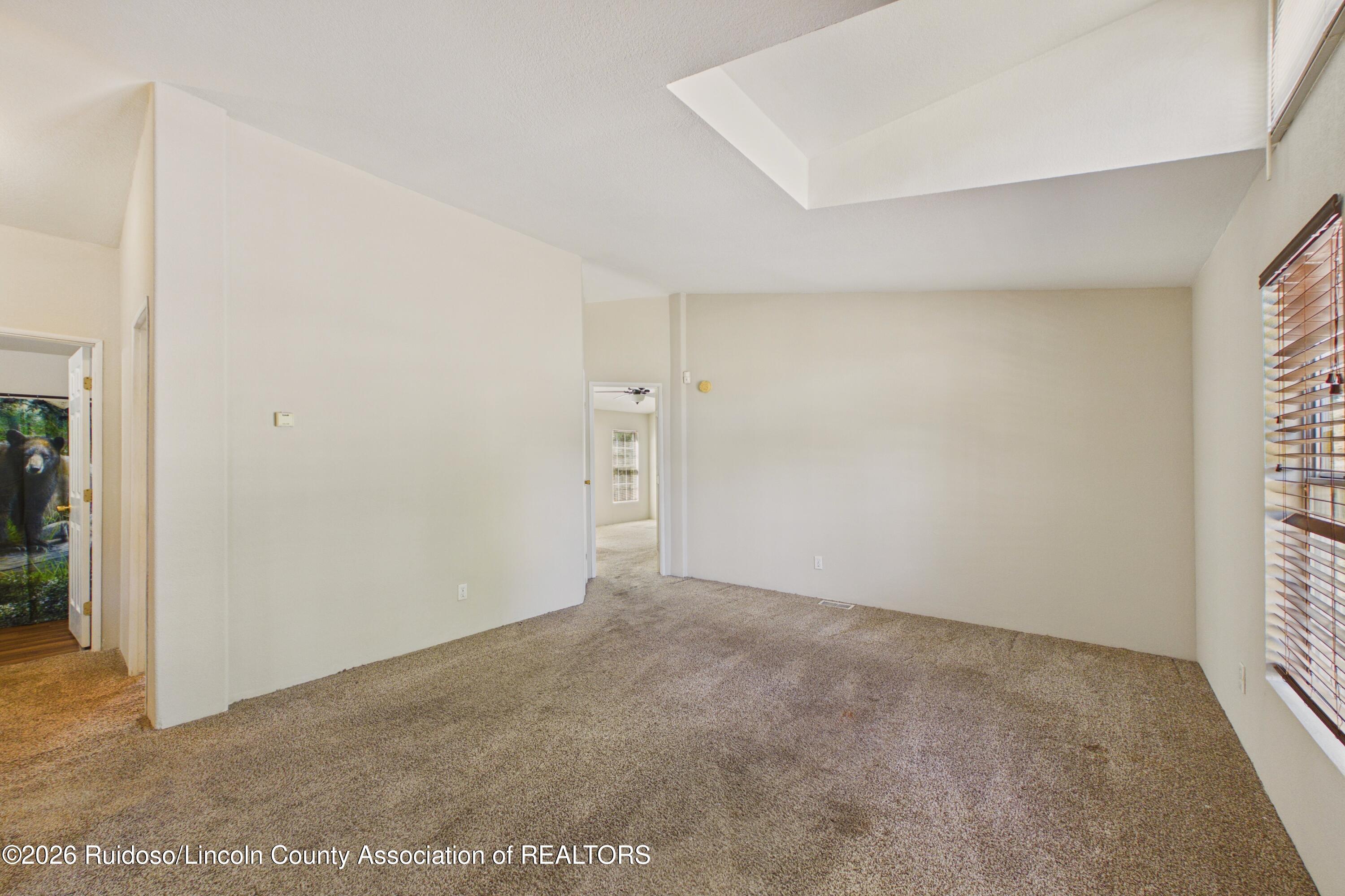Empty carpeted room with a recessed ceiling and a window with wooden blinds.
