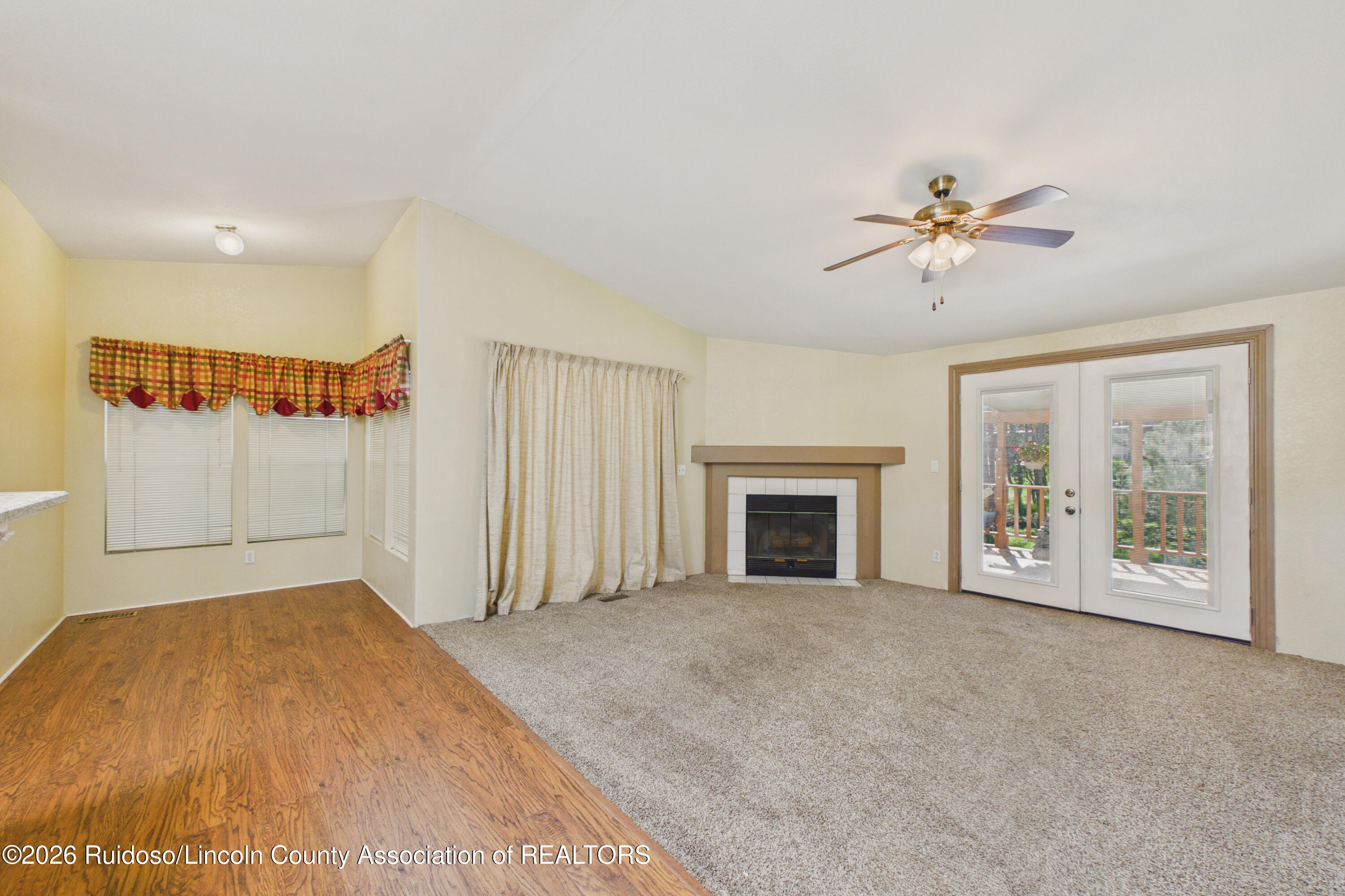 Unfurnished living room with a corner fireplace, ceiling fan, and French doors opening to a deck.