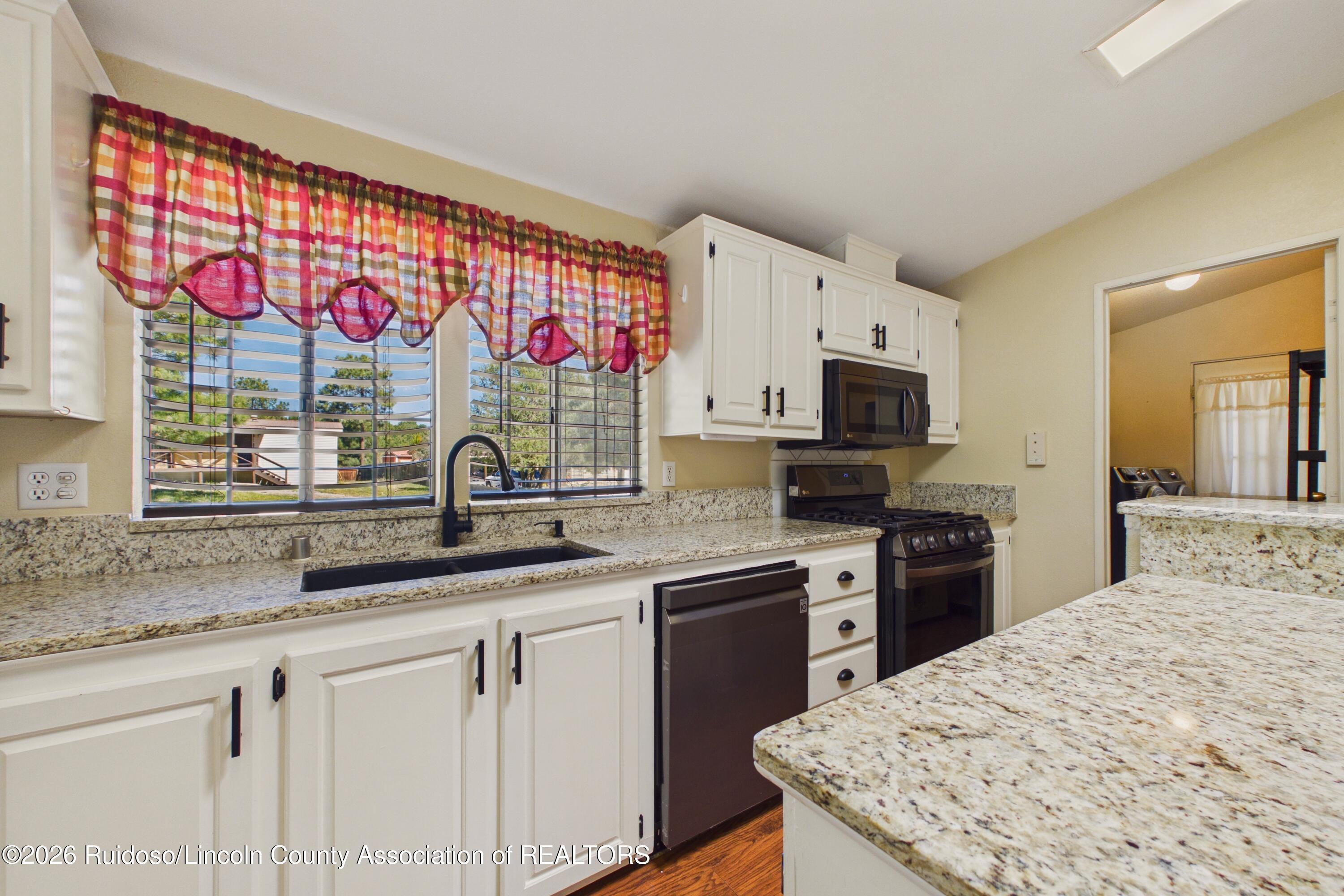 Kitchen with white cabinets, granite counters, black appliances, and colorful plaid curtains.