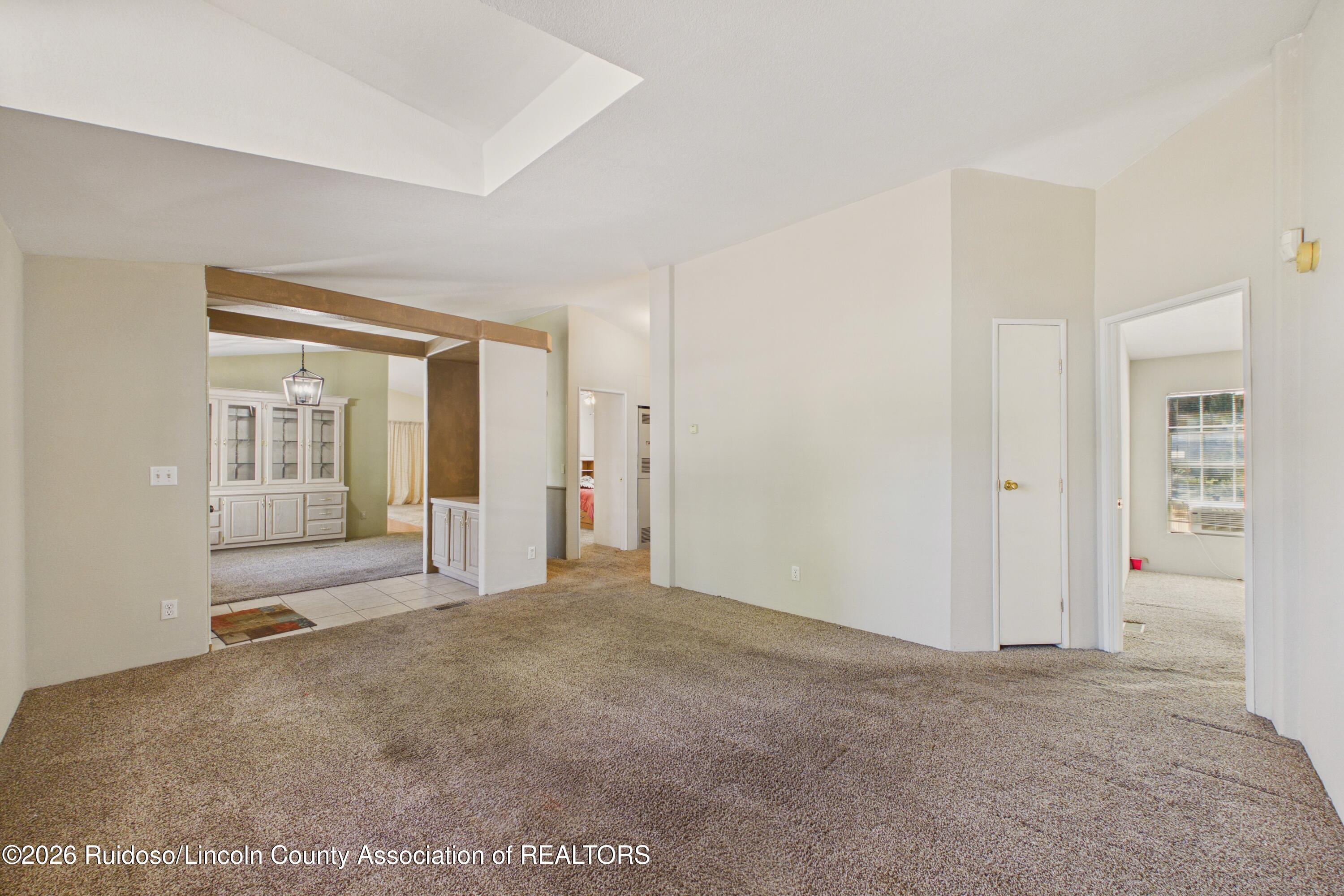 Mostly vacant living room with beige carpet, a tray ceiling, and exposed wood beams.