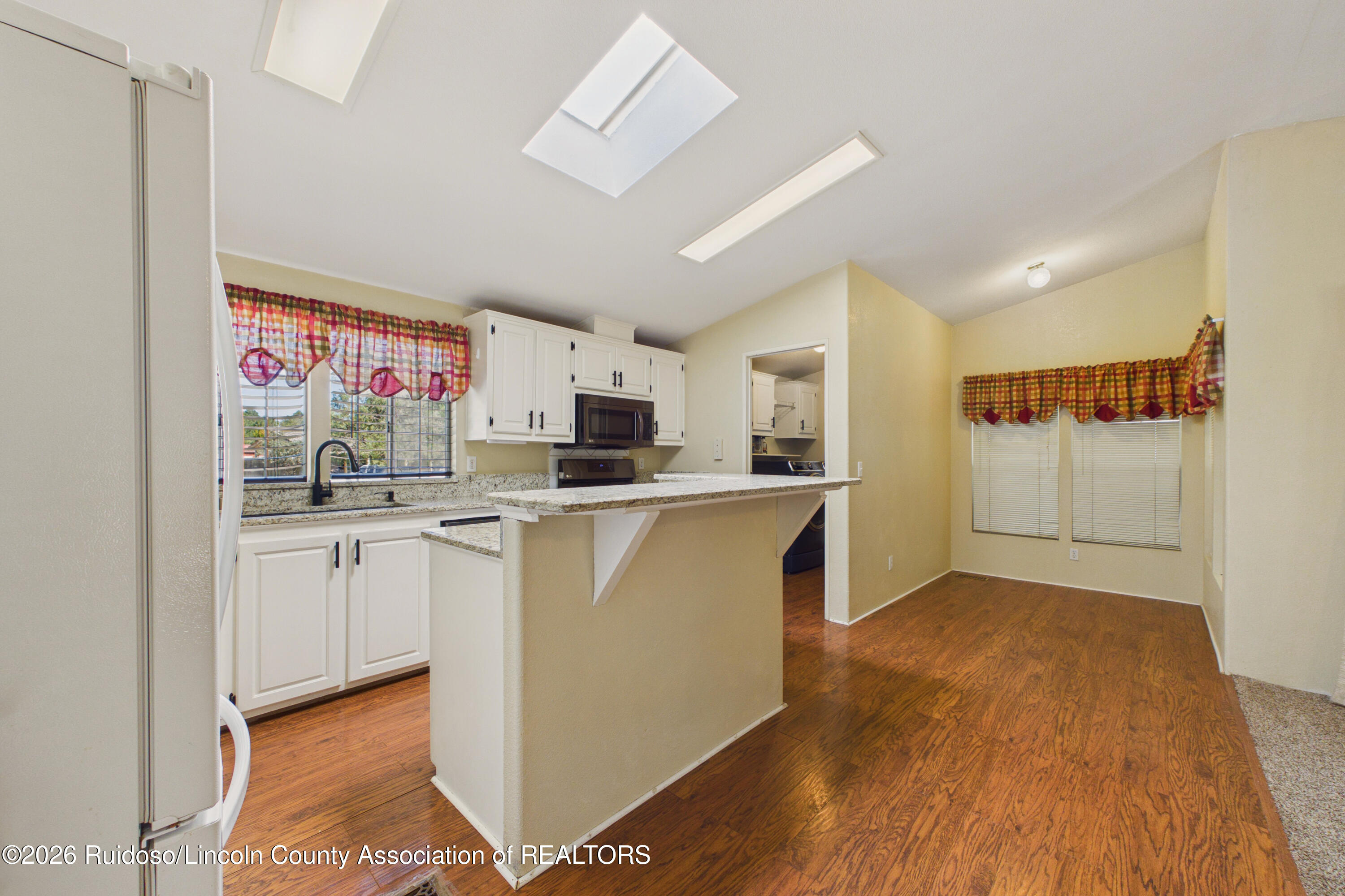Kitchen and dining area with white cabinets, granite peninsula, wood floors, and a skylight.