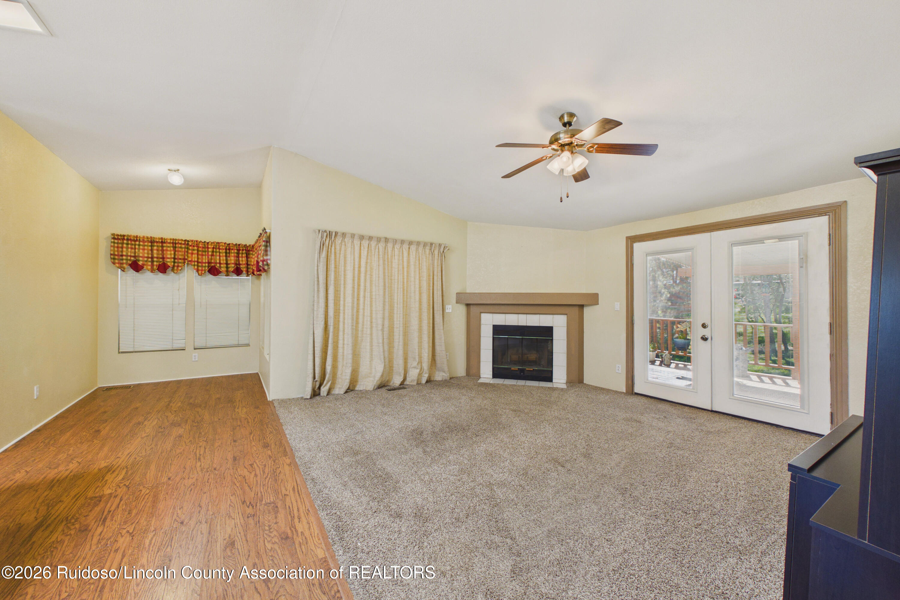 Empty living room with a tiled fireplace, ceiling fan, and glass doors to a deck.