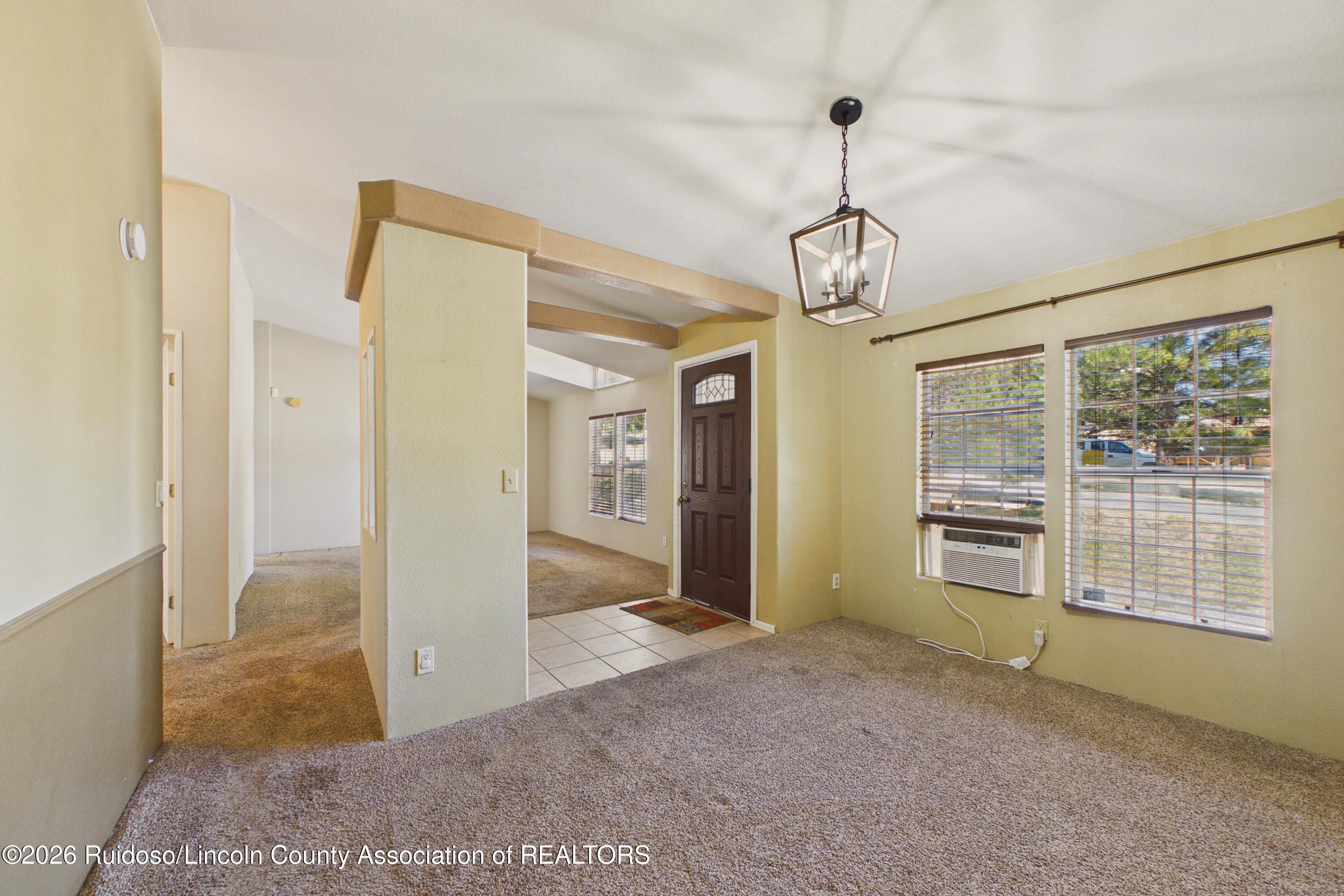 Vacant carpeted living area with a tiled entry, dark front door, hanging lantern, and window air conditioner.