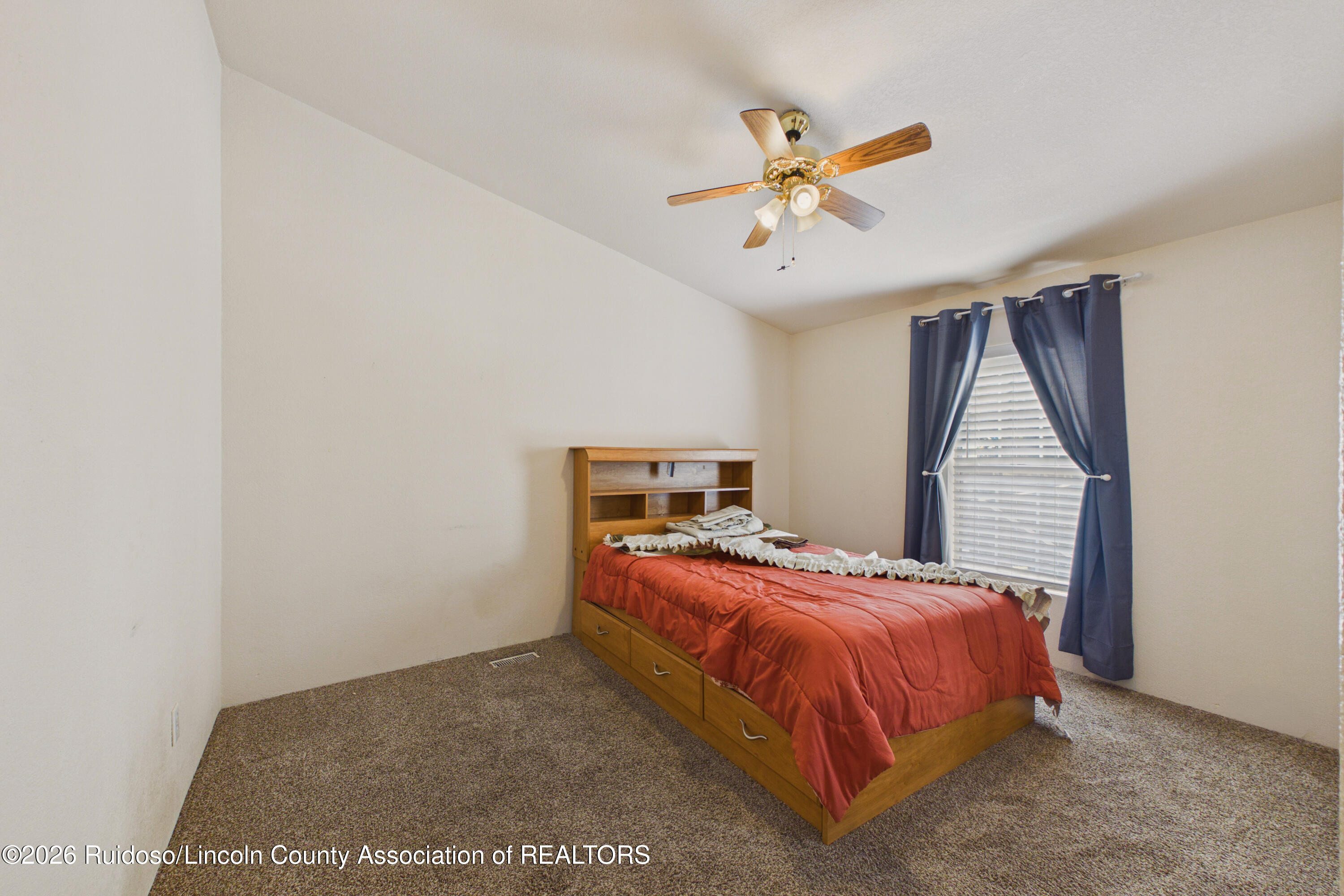 Bedroom with a wooden bed, red bedspread, ceiling fan, and navy curtains.