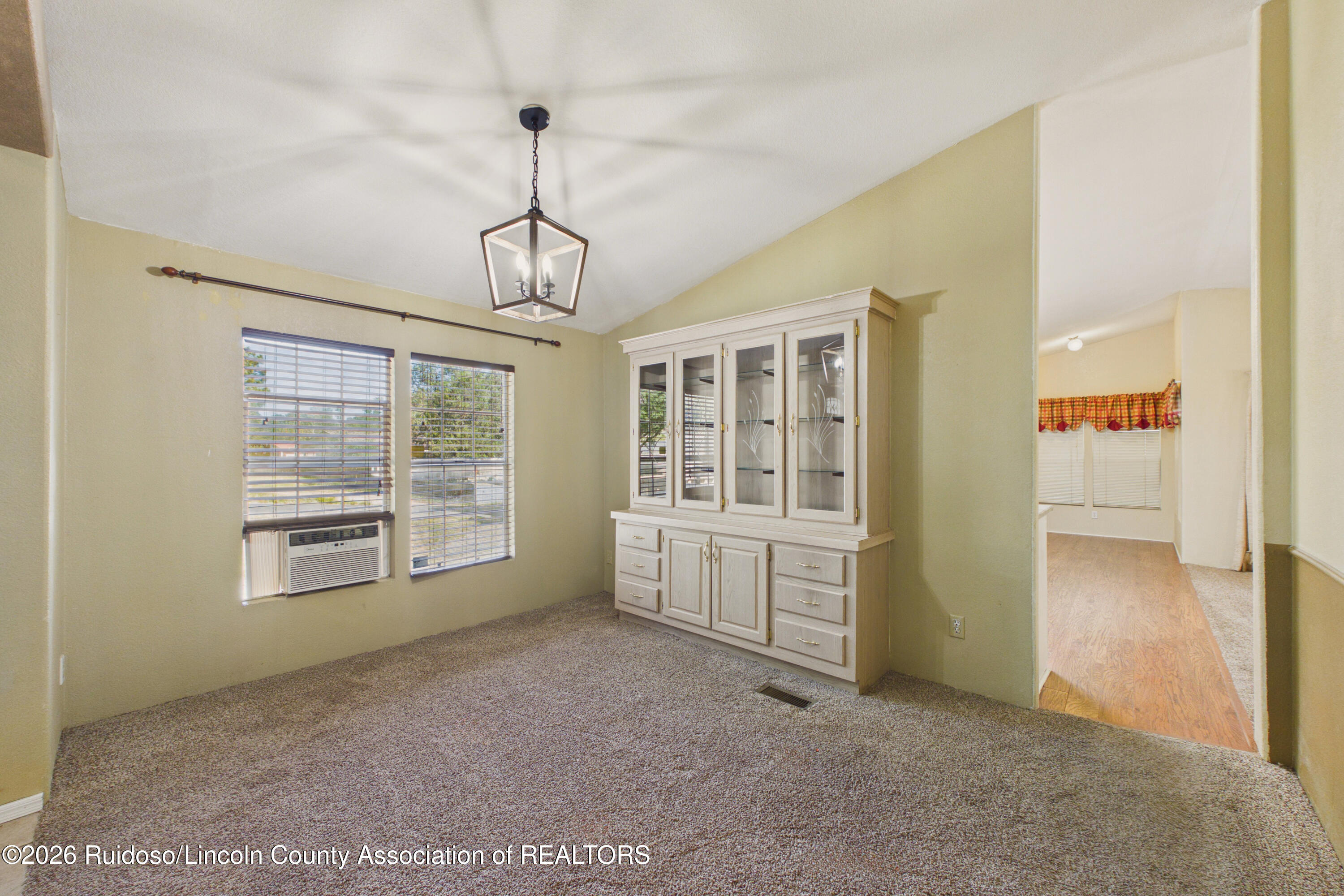 Unfurnished dining room with a built-in glass-front cabinet, carpet, and windows with blinds.