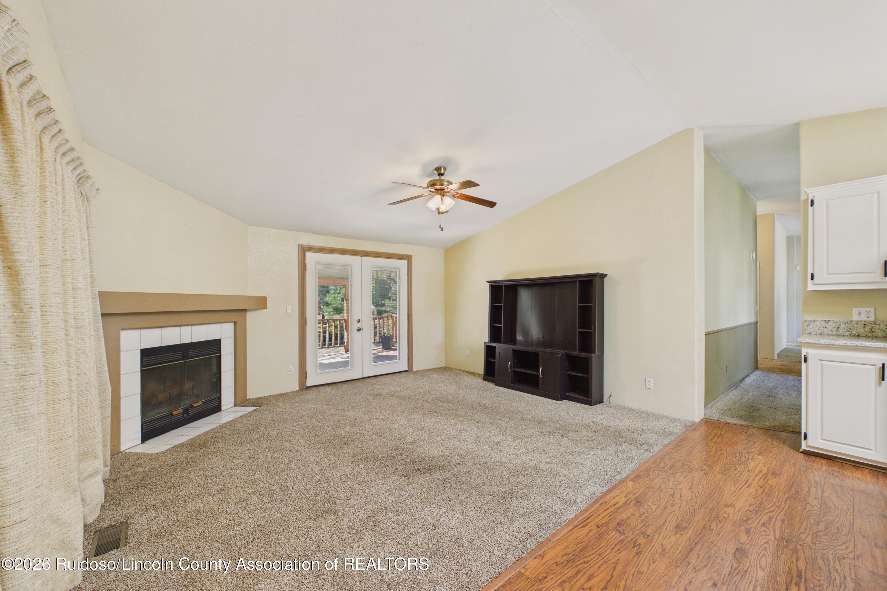 Living room with a tiled fireplace, deck doors, ceiling fan, and dark media cabinet.
