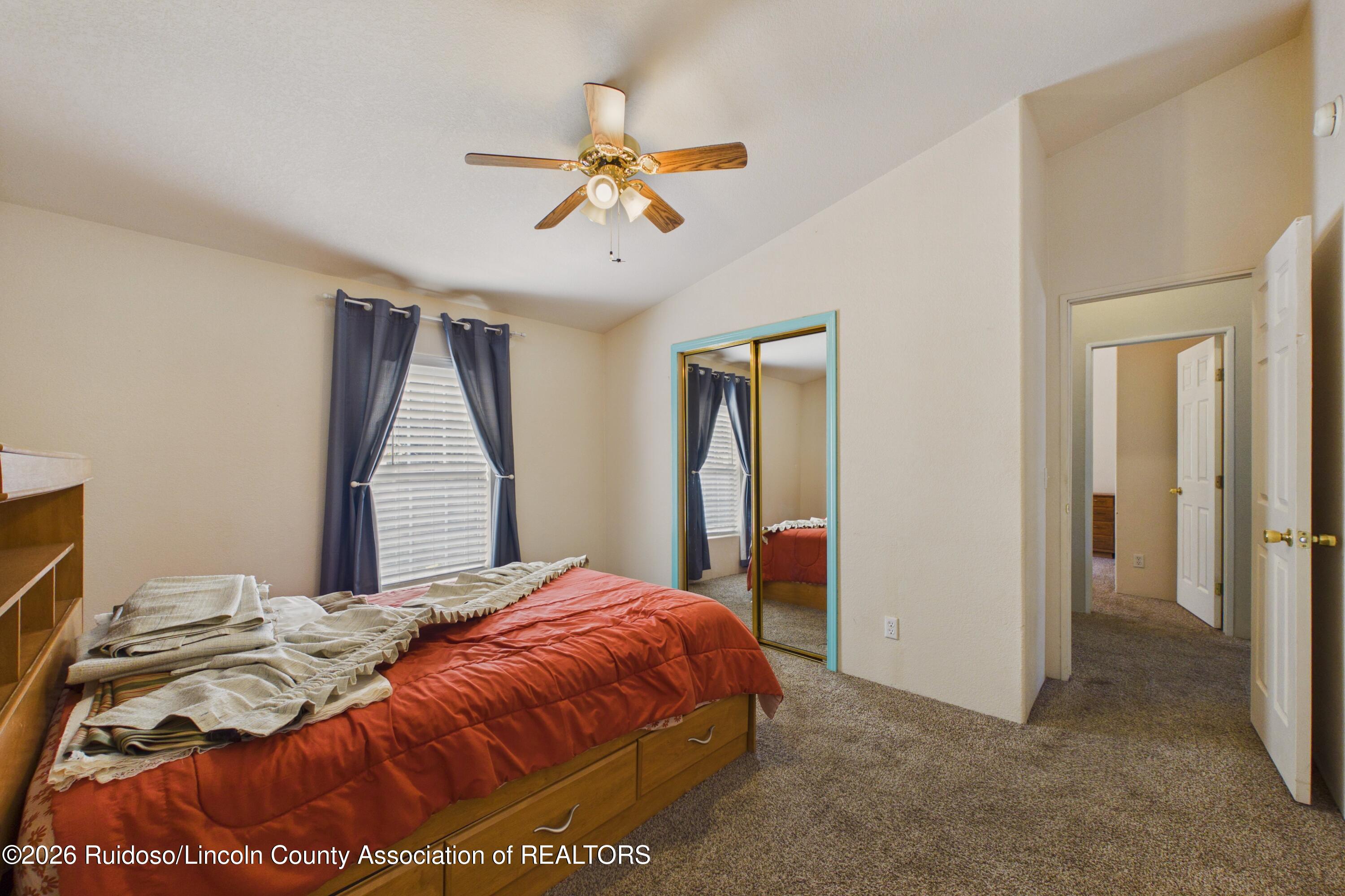 Bedroom with a red quilted bed, blue curtains, mirrored closet doors, and a ceiling fan.