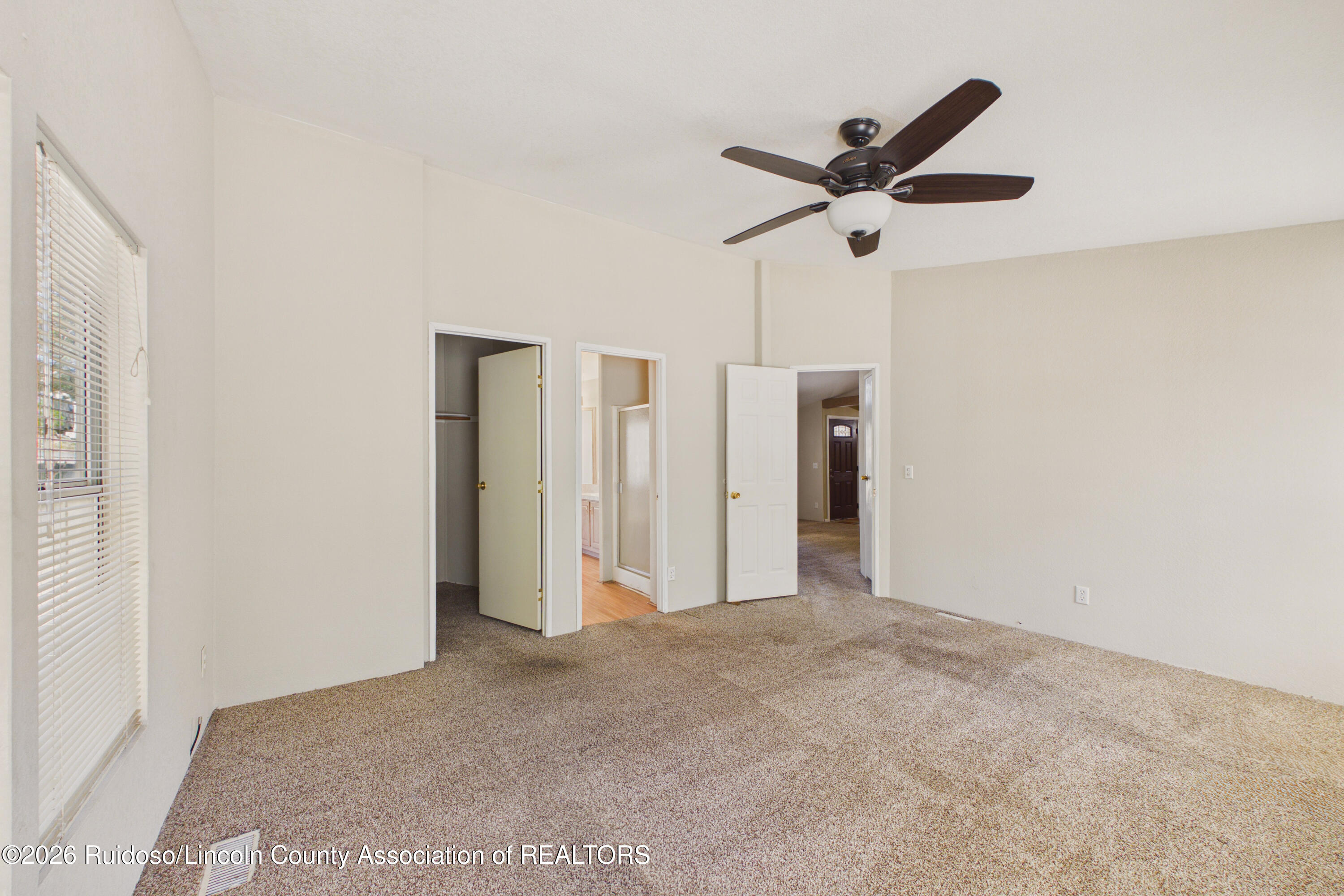 Empty carpeted bedroom with a dark-bladed ceiling fan and window blinds.