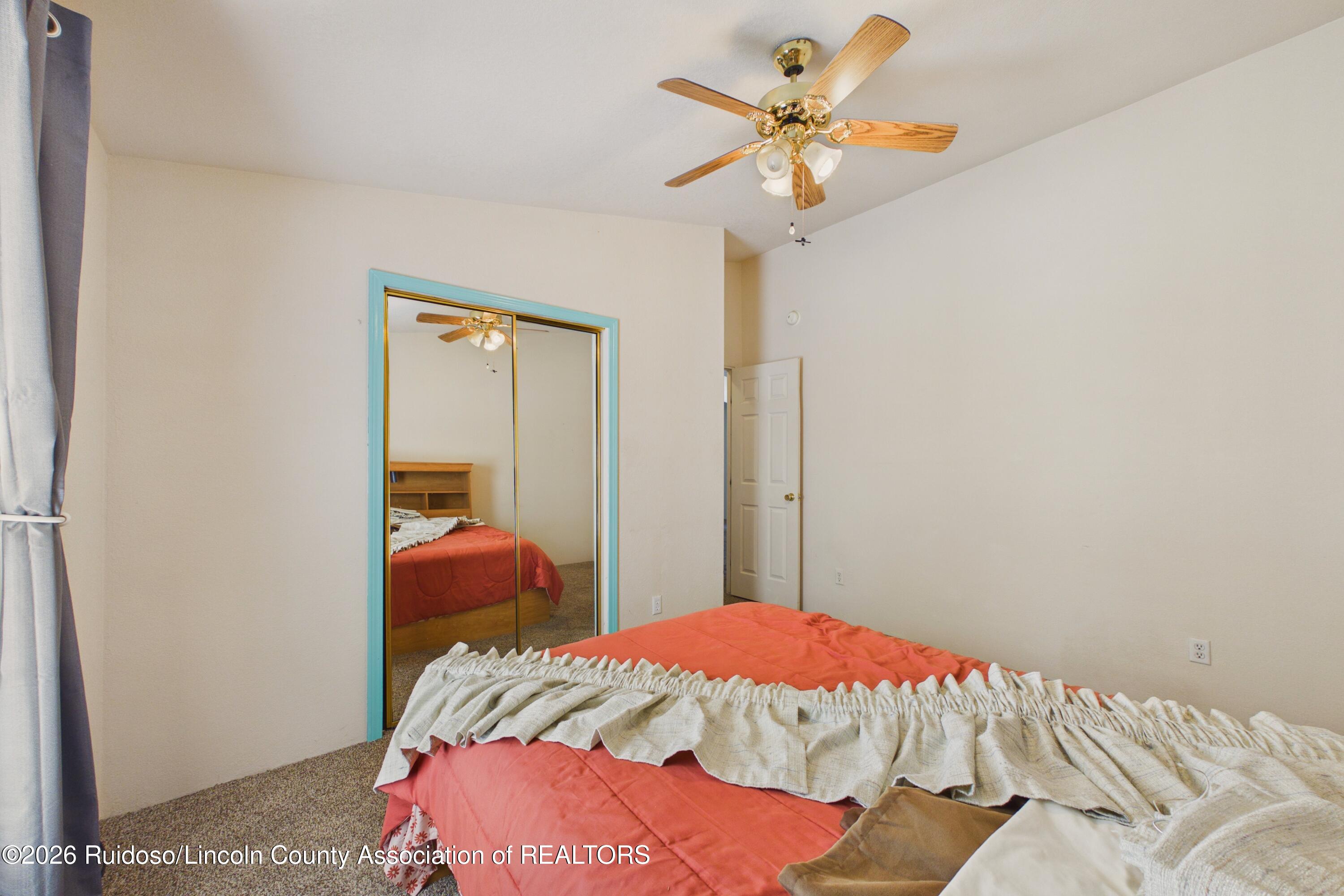 Furnished bedroom with a coral bedspread, turquoise-trimmed mirrored closet doors, and a ceiling fan.