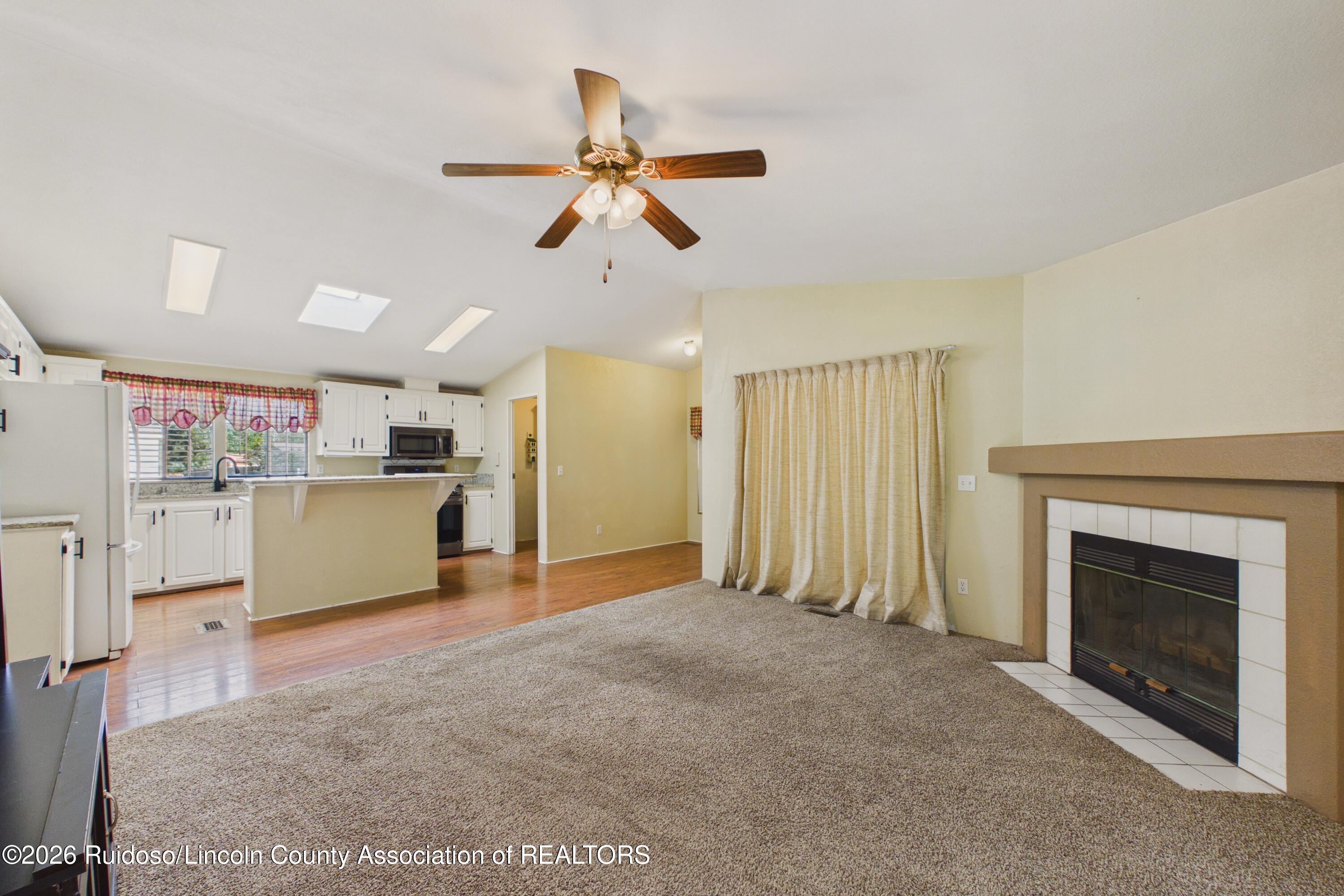 Vacant living room opening to a kitchen, with a tiled fireplace and breakfast bar.