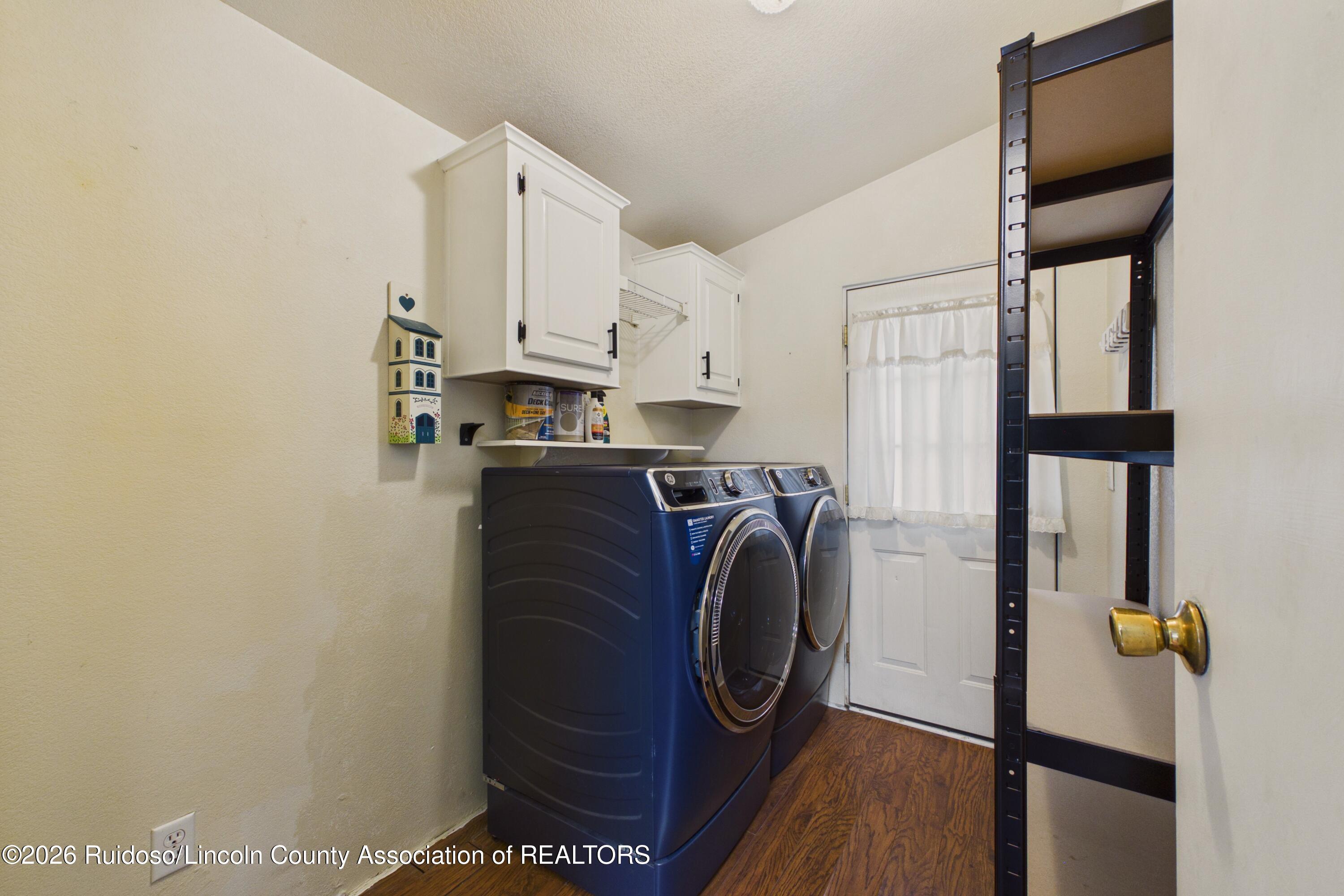 Laundry room with blue front-loading washer and dryer, white cabinets, and a tall storage rack.