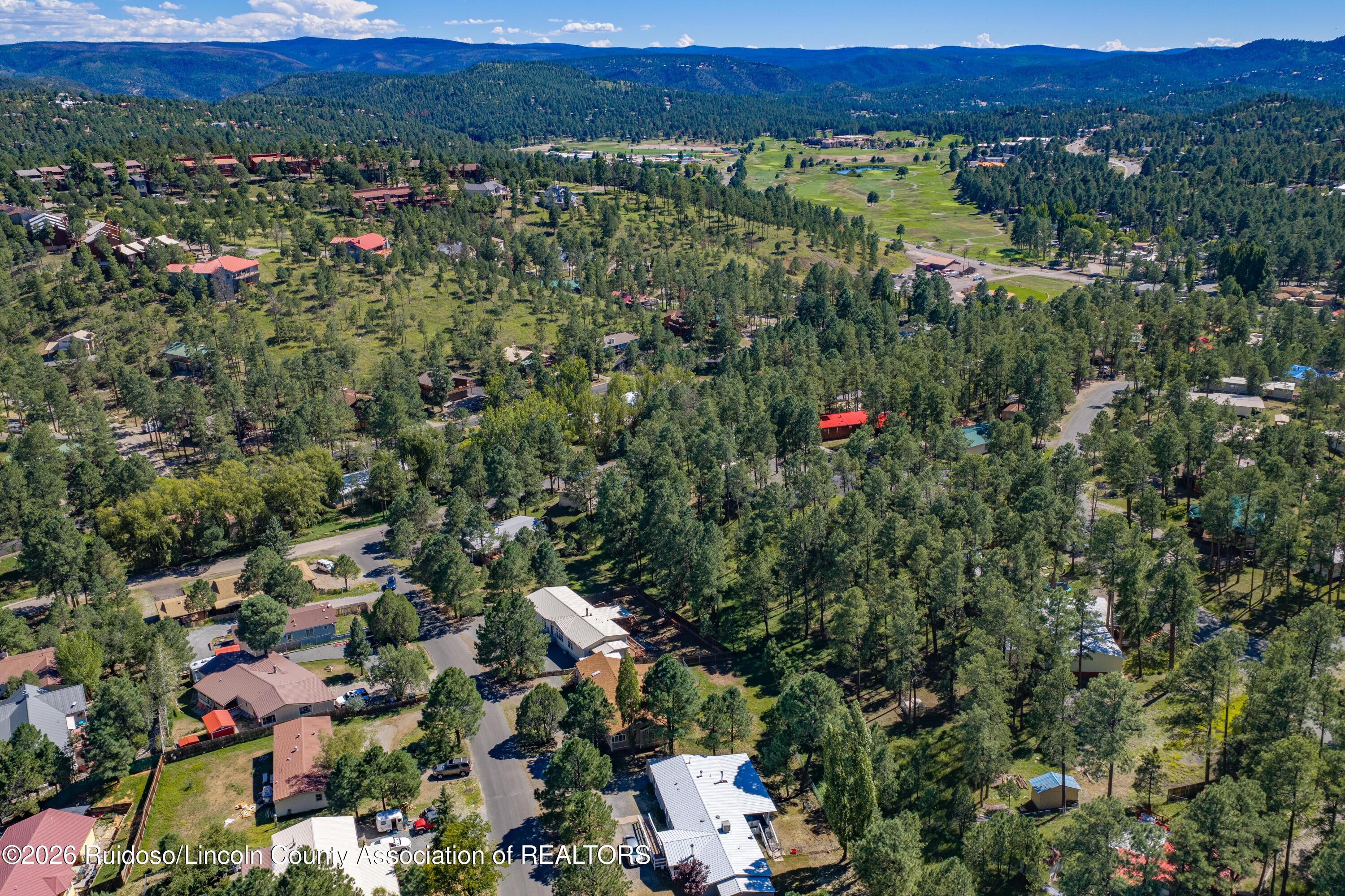 Aerial view of a wooded Ruidoso neighborhood, with a golf course and mountain ridges beyond.
