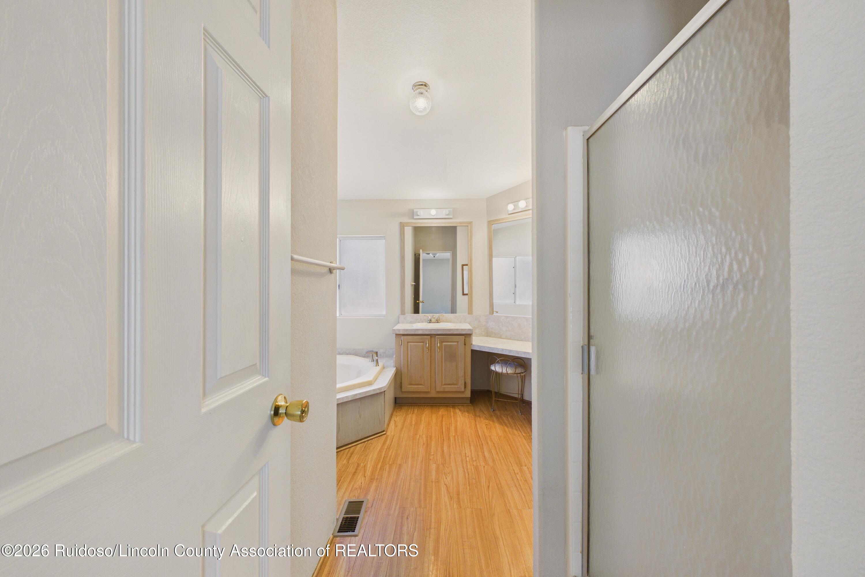 Bathroom with a corner soaking tub, wood-finish vanity, large mirrors, and wood-look flooring.
