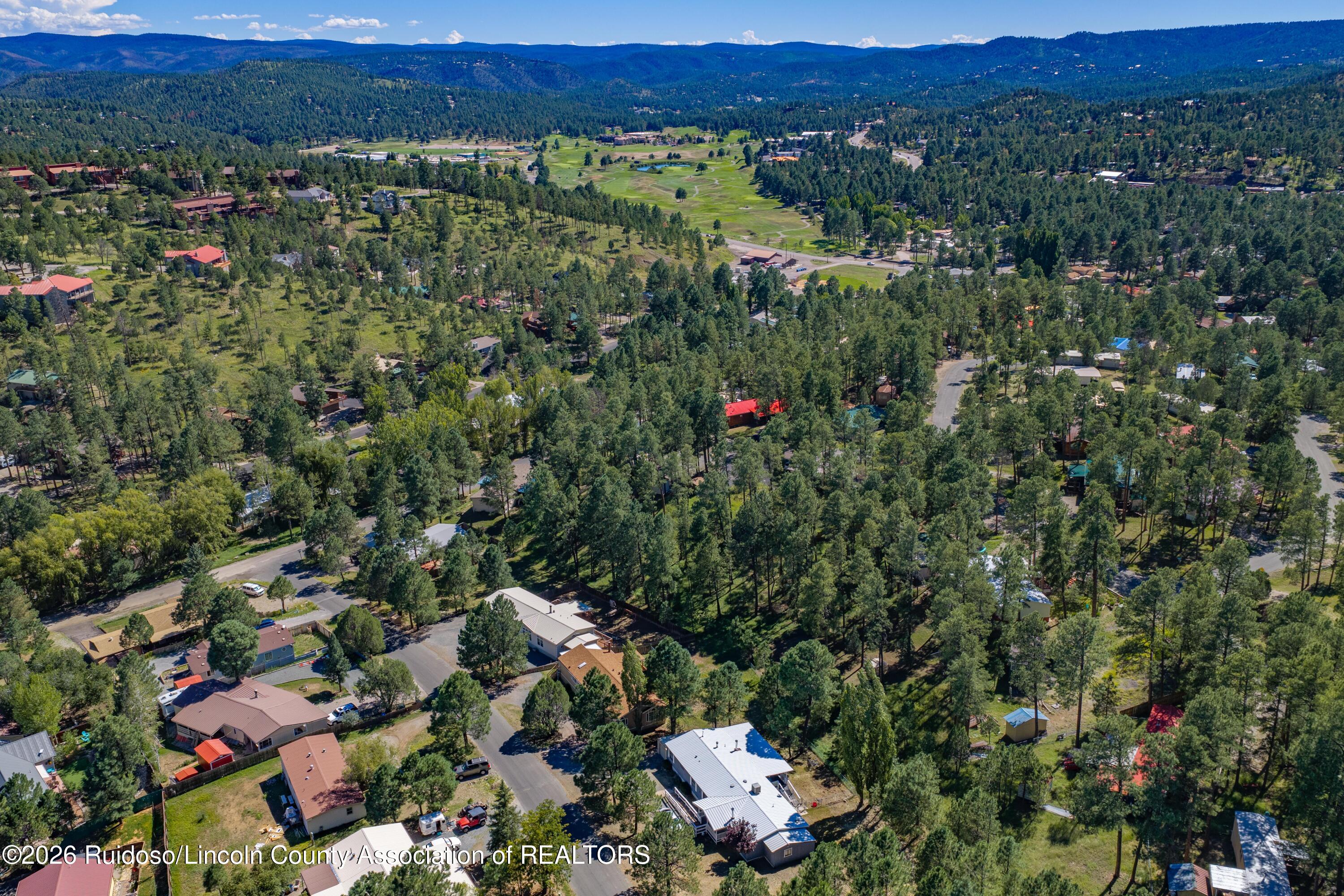Aerial view of a wooded neighborhood, golf course, and distant mountain ridges.