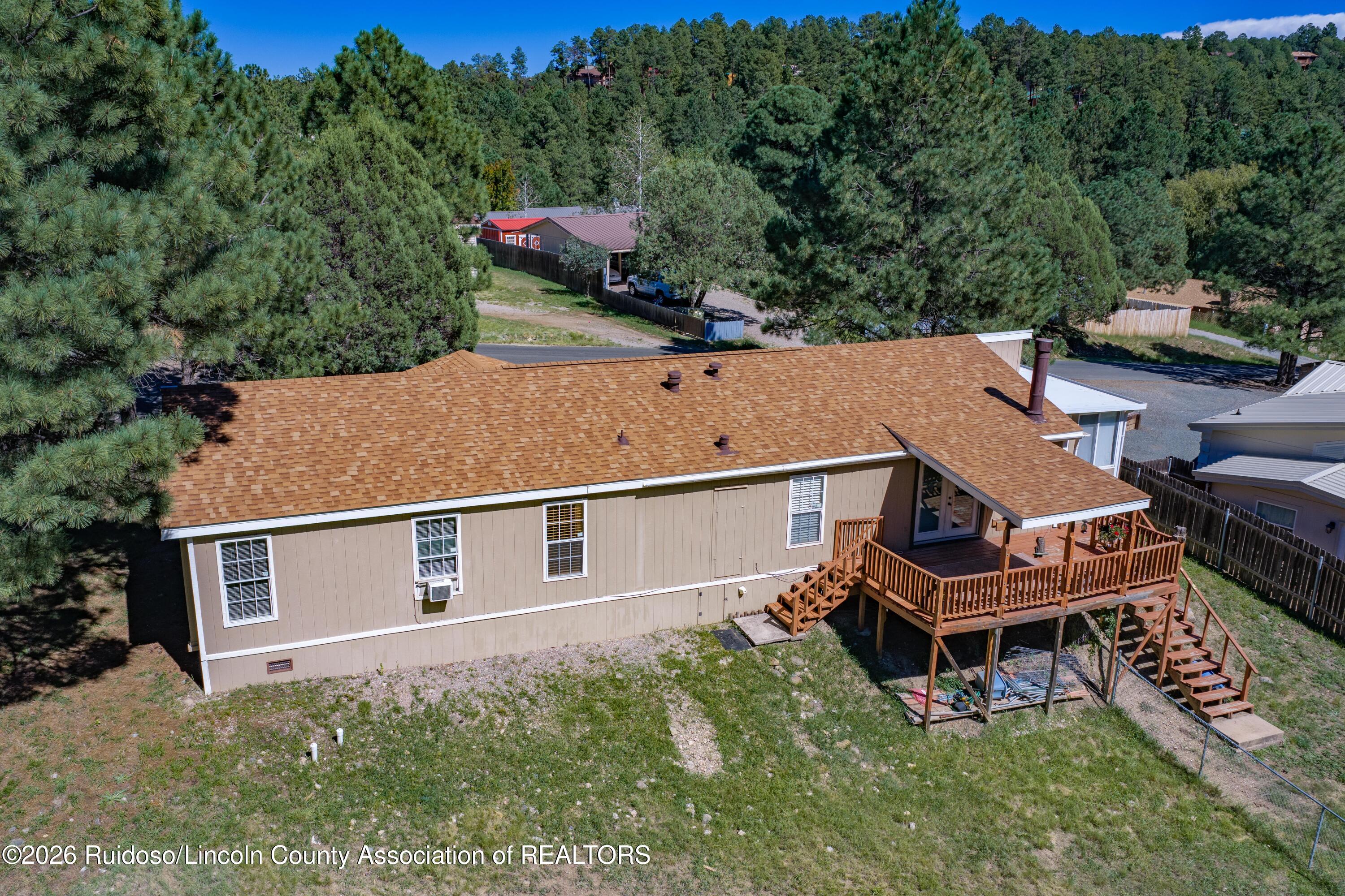 Aerial view of a tan home with a large raised wooden deck among pine trees.