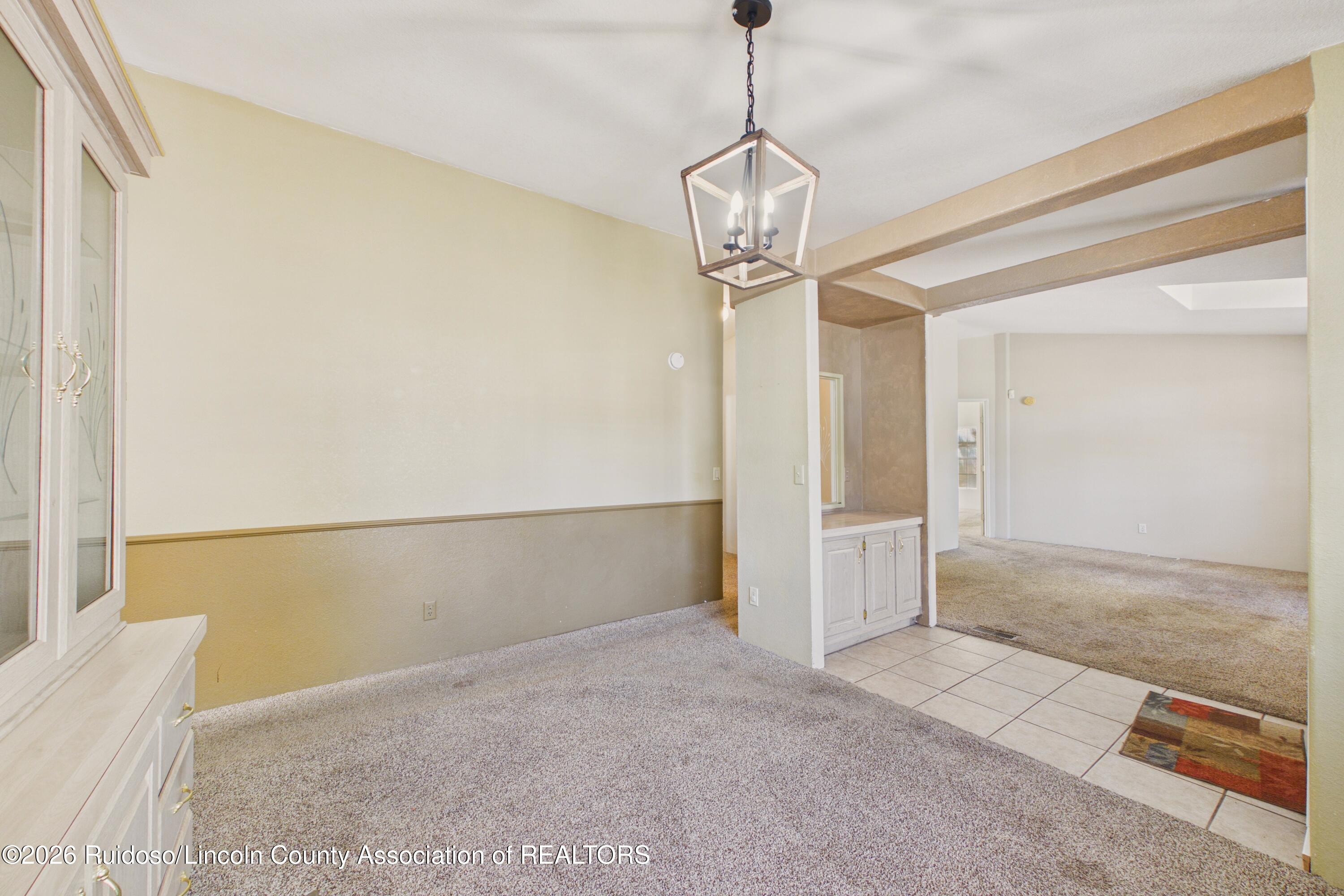 Empty dining area with a geometric chandelier, built-in cabinet, and tiled threshold to the adjoining room.