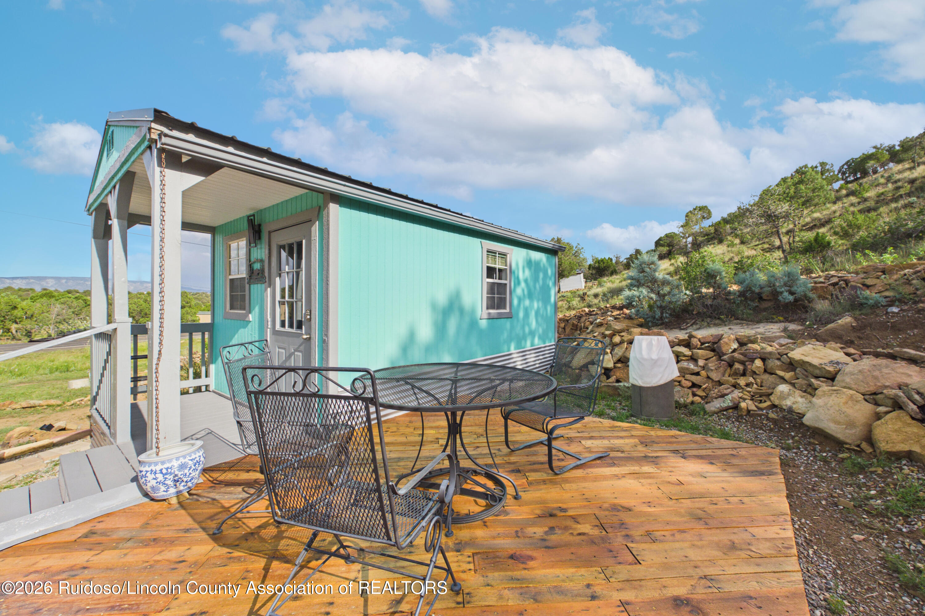 Turquoise home with a covered porch and wooden deck furnished with a black metal patio set.