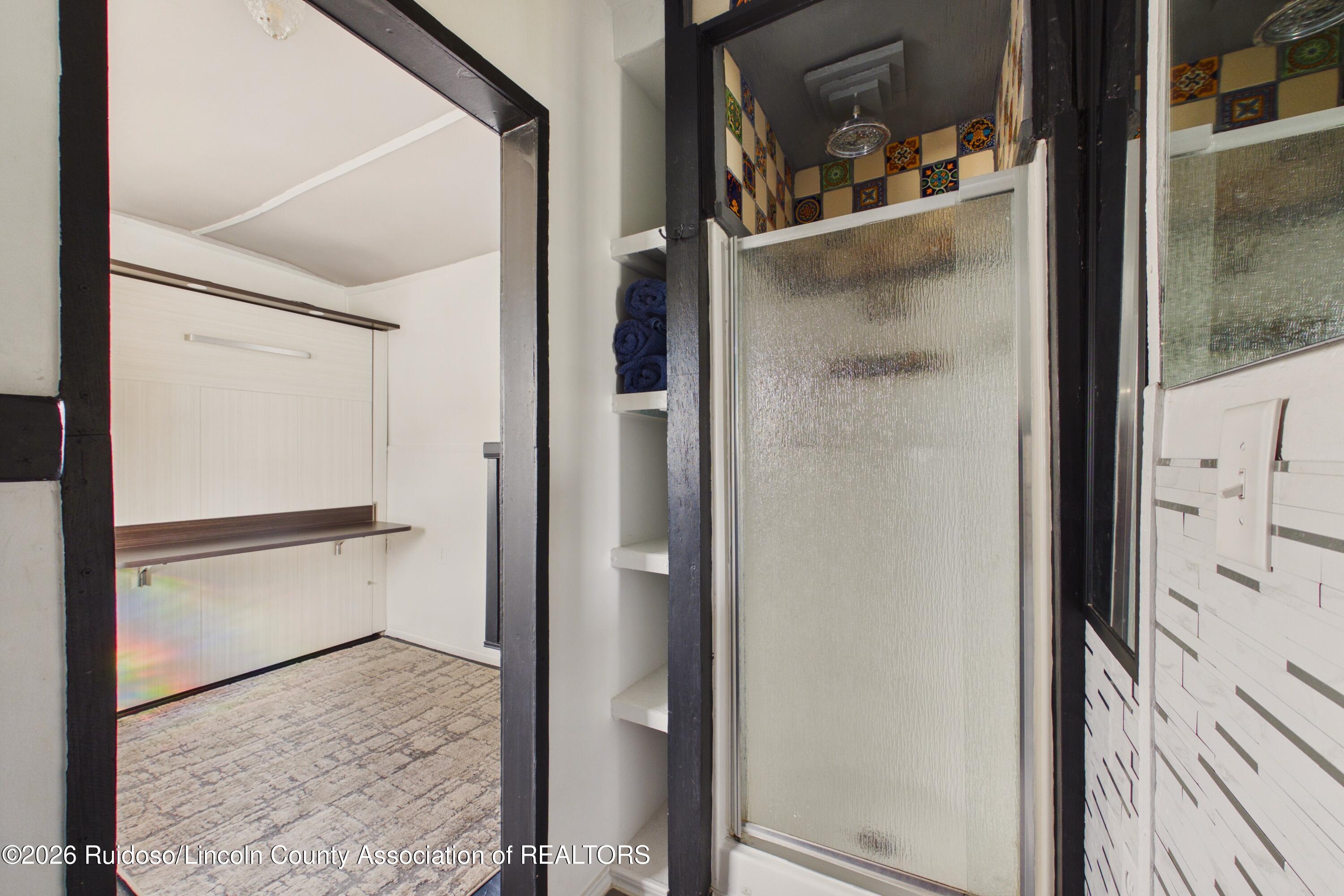 Bathroom with frosted-glass shower, colorful tile, built-in towel shelves, and an adjacent vanity area.