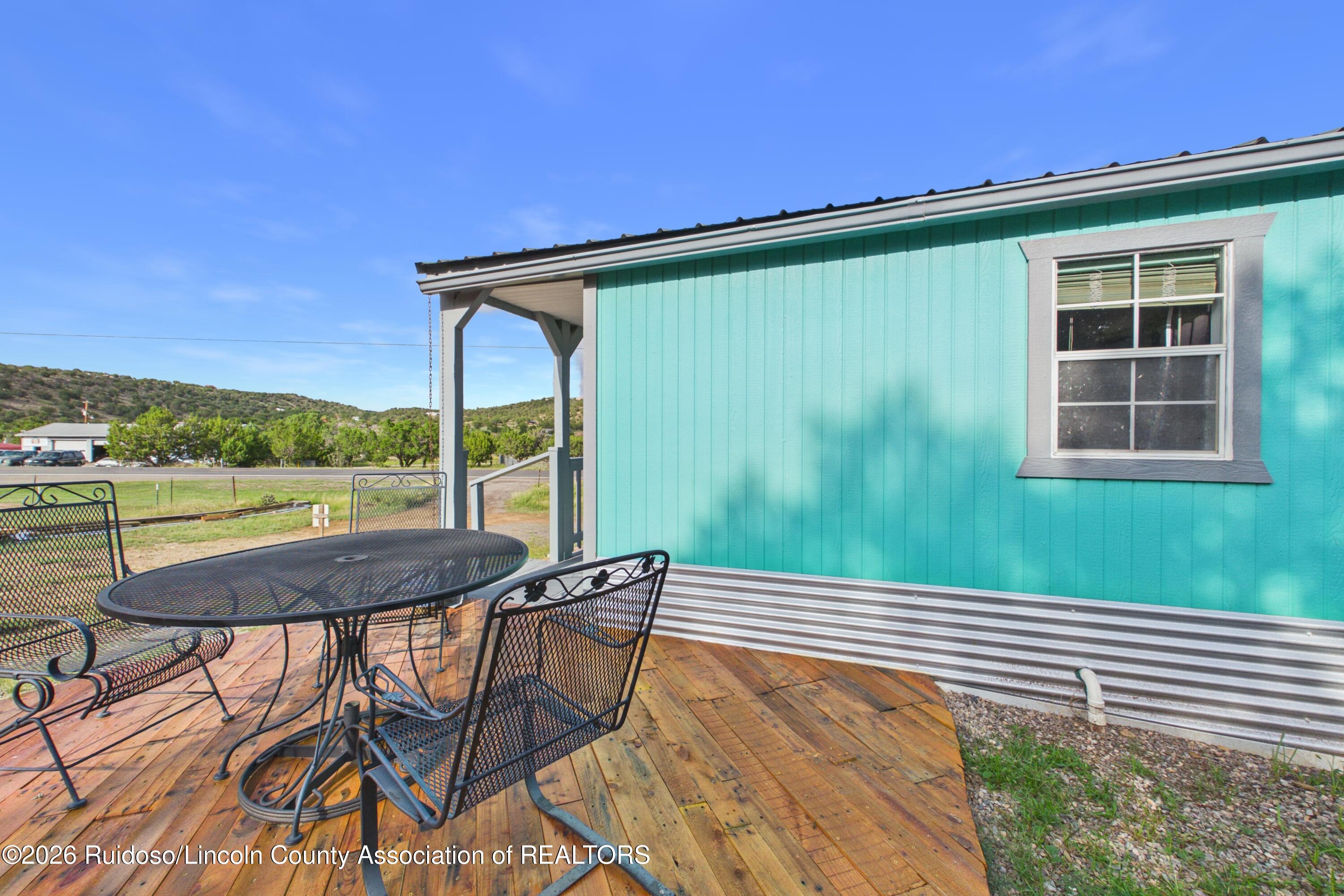 Turquoise-sided property beside a wooden deck with black metal patio furniture and a covered entry.