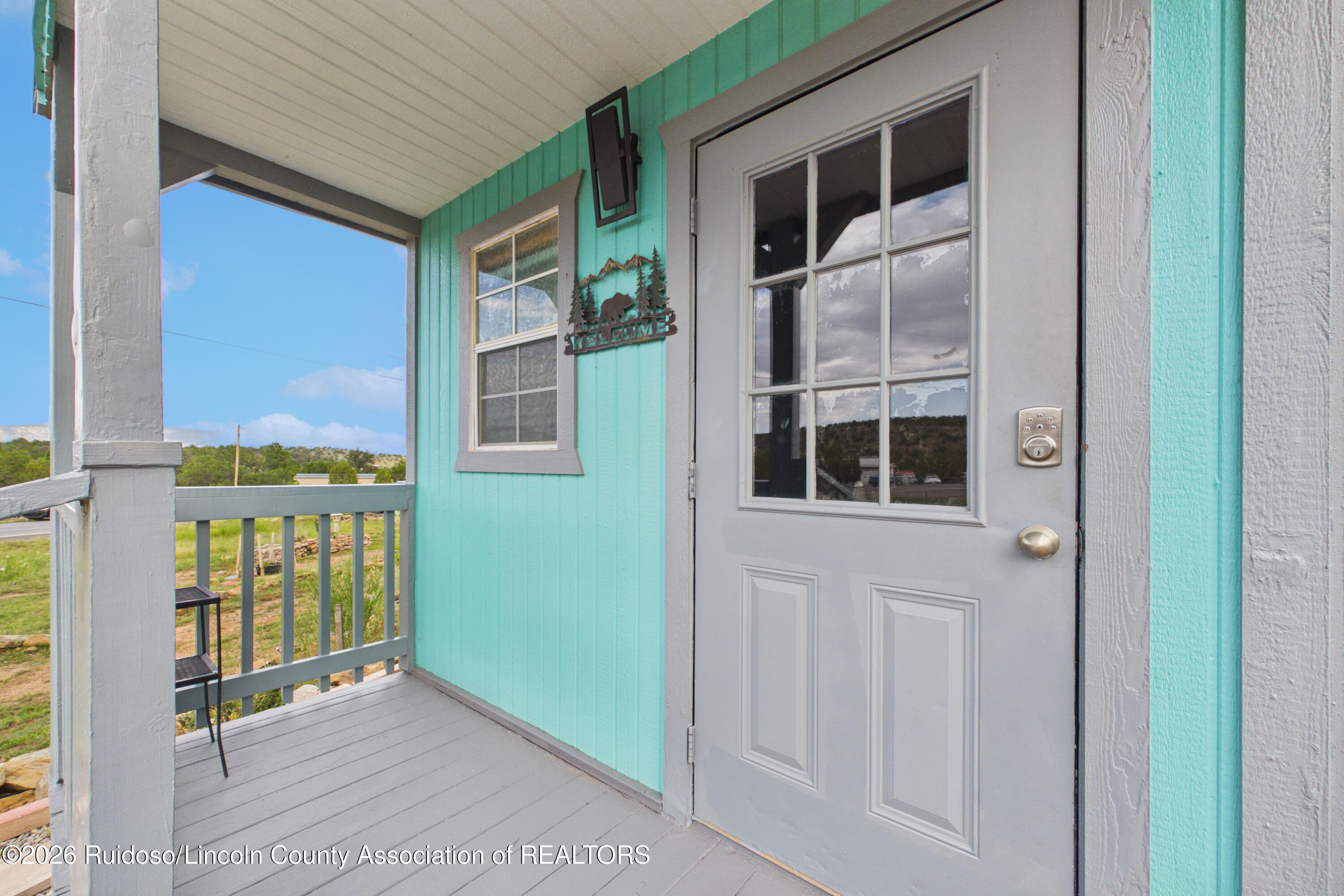 Covered porch with turquoise siding, gray front door, and a bear-and-mountain welcome sign.