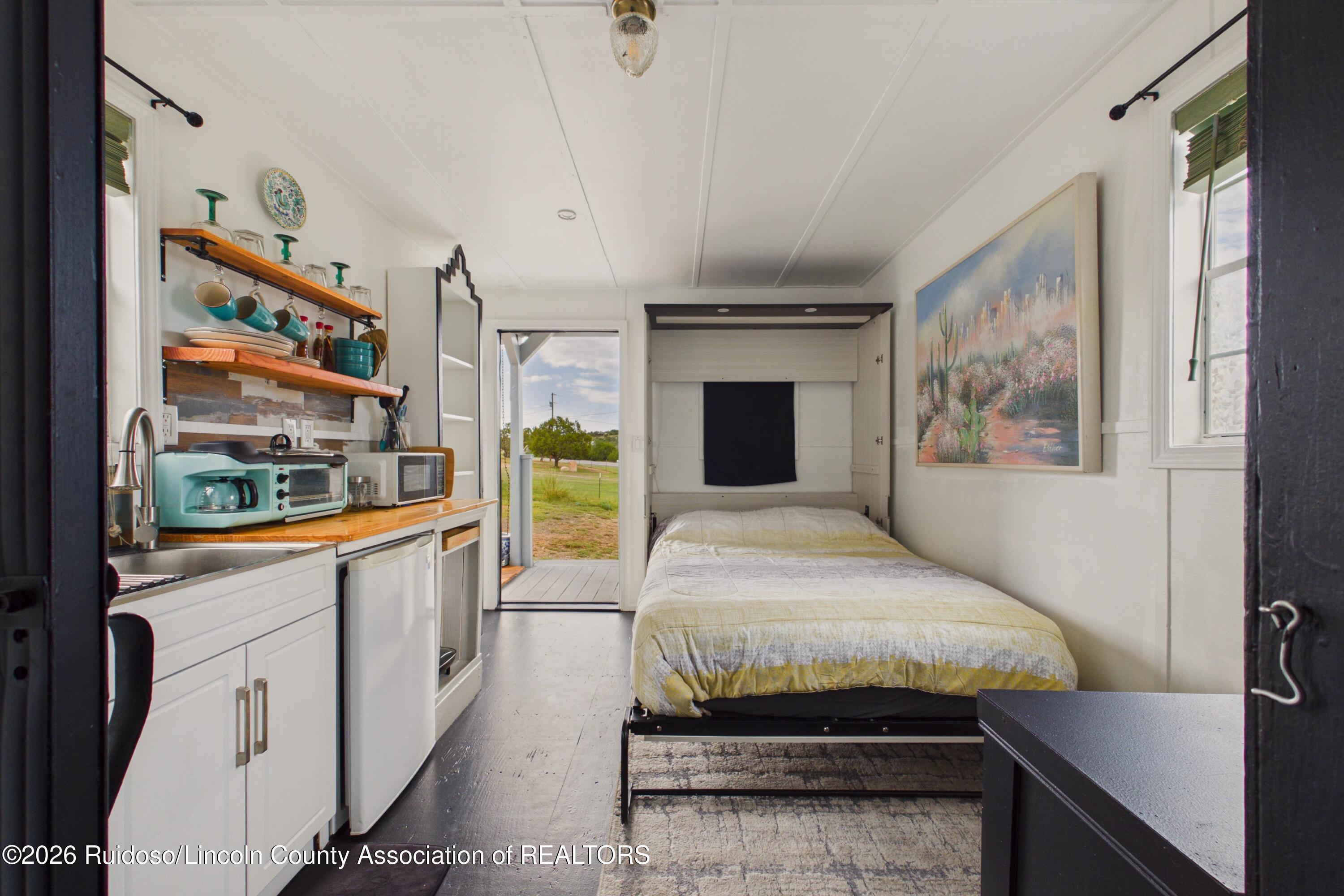 Compact bedroom with a fold-down bed, kitchenette, and open doorway to a grassy outdoor area.