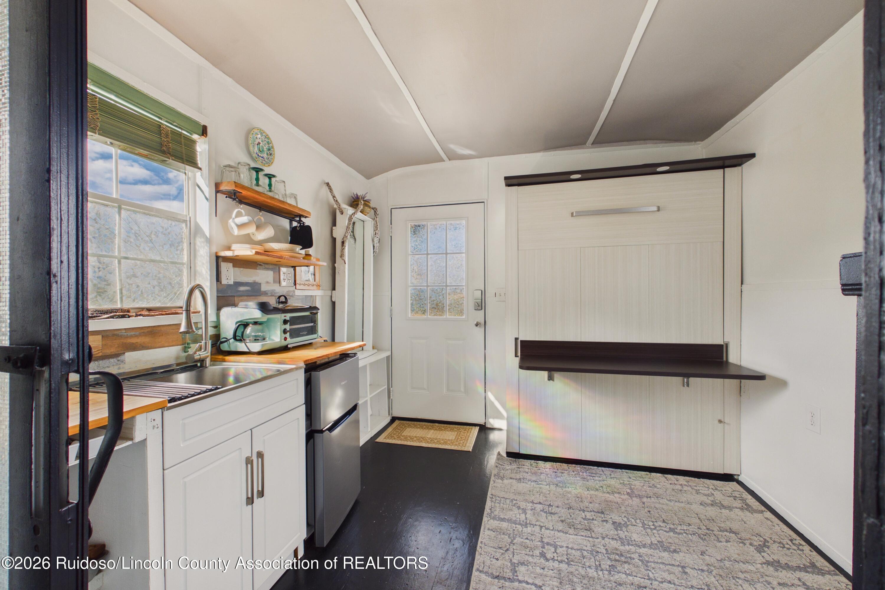 Compact kitchen with white cabinets, wood shelves, and a fold-down wall bed.