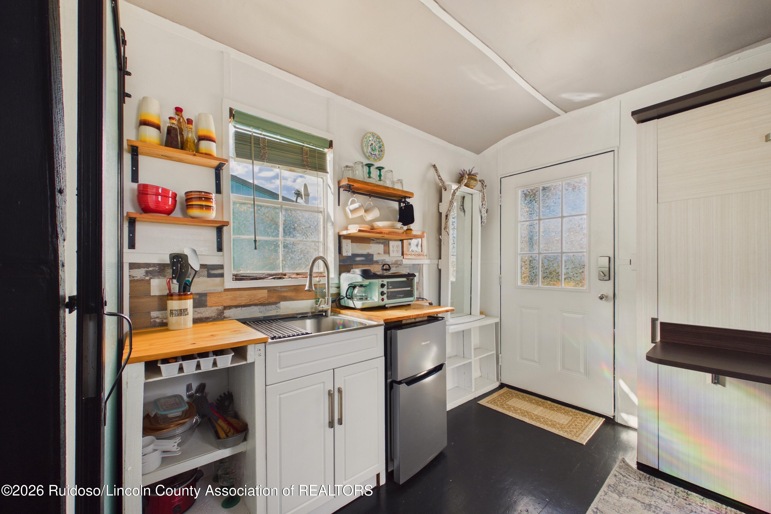 Compact kitchen with wood countertops, open shelves, and a glass-paneled entry door.