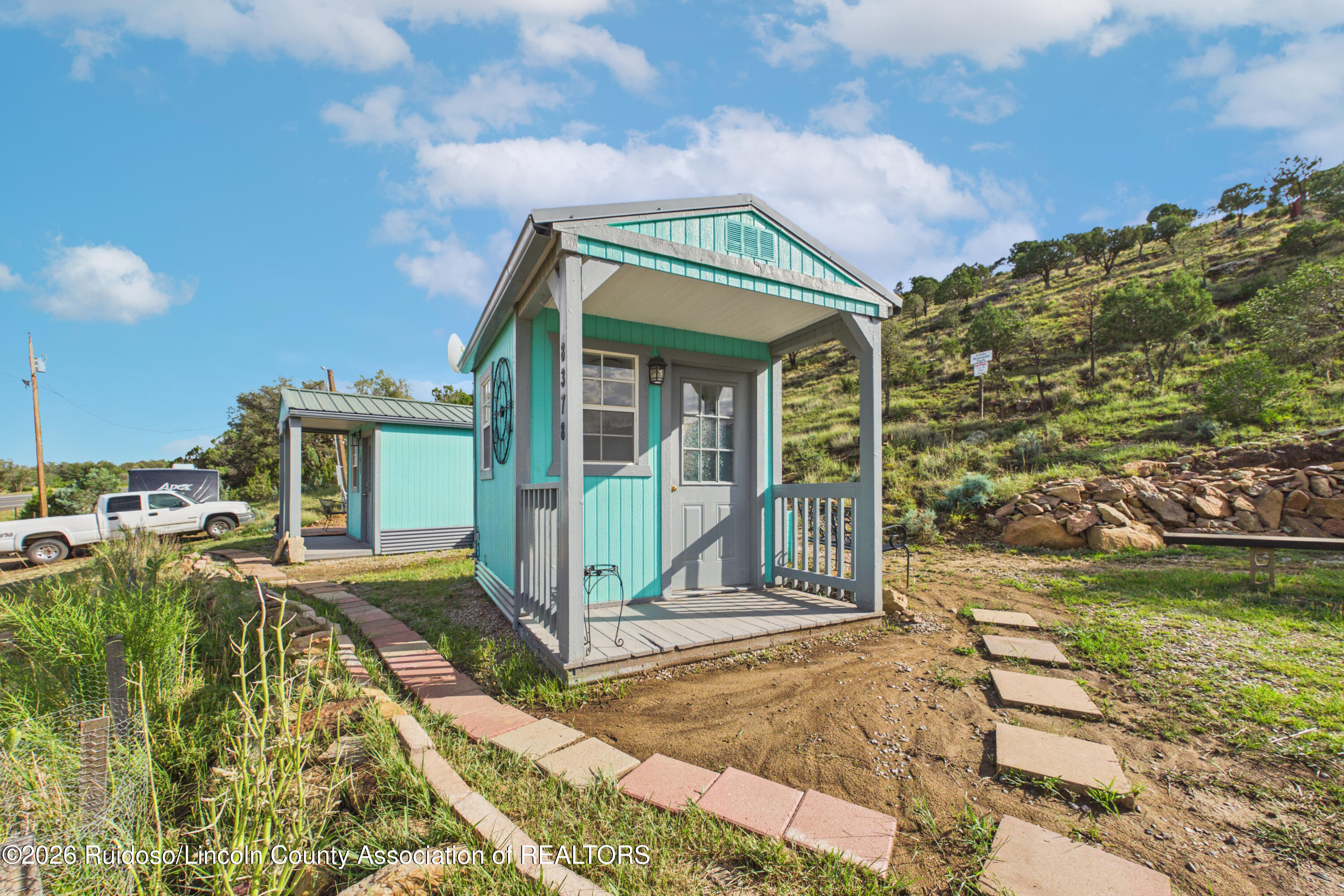 Turquoise building with a covered porch beside a rocky, tree-dotted hillside.